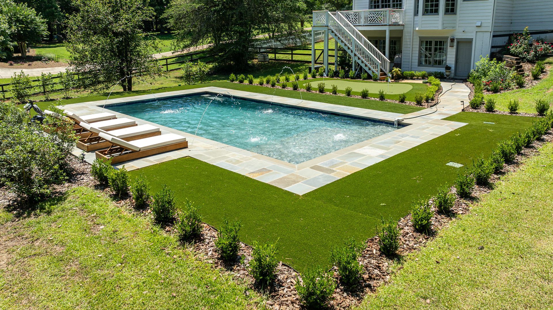 Backyard pool with stone patio, lounge chairs, and manicured lawn beside a house