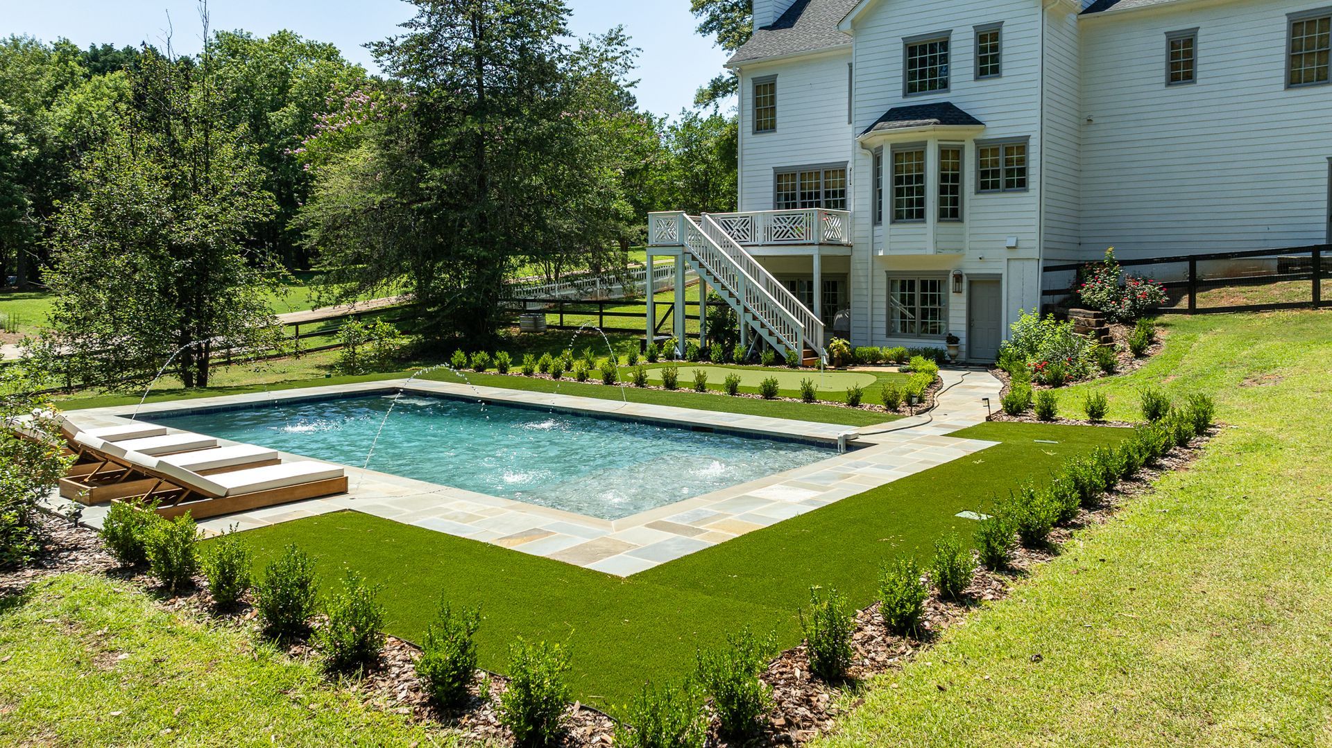Backyard with rectangular in-ground pool beside a white house and landscaped lawn
