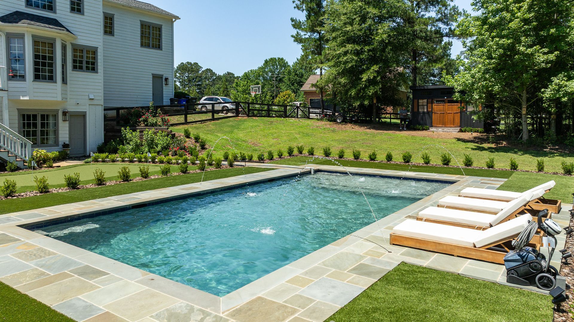 Backyard swimming pool with lounge chairs beside a house and green lawn on a sunny day
