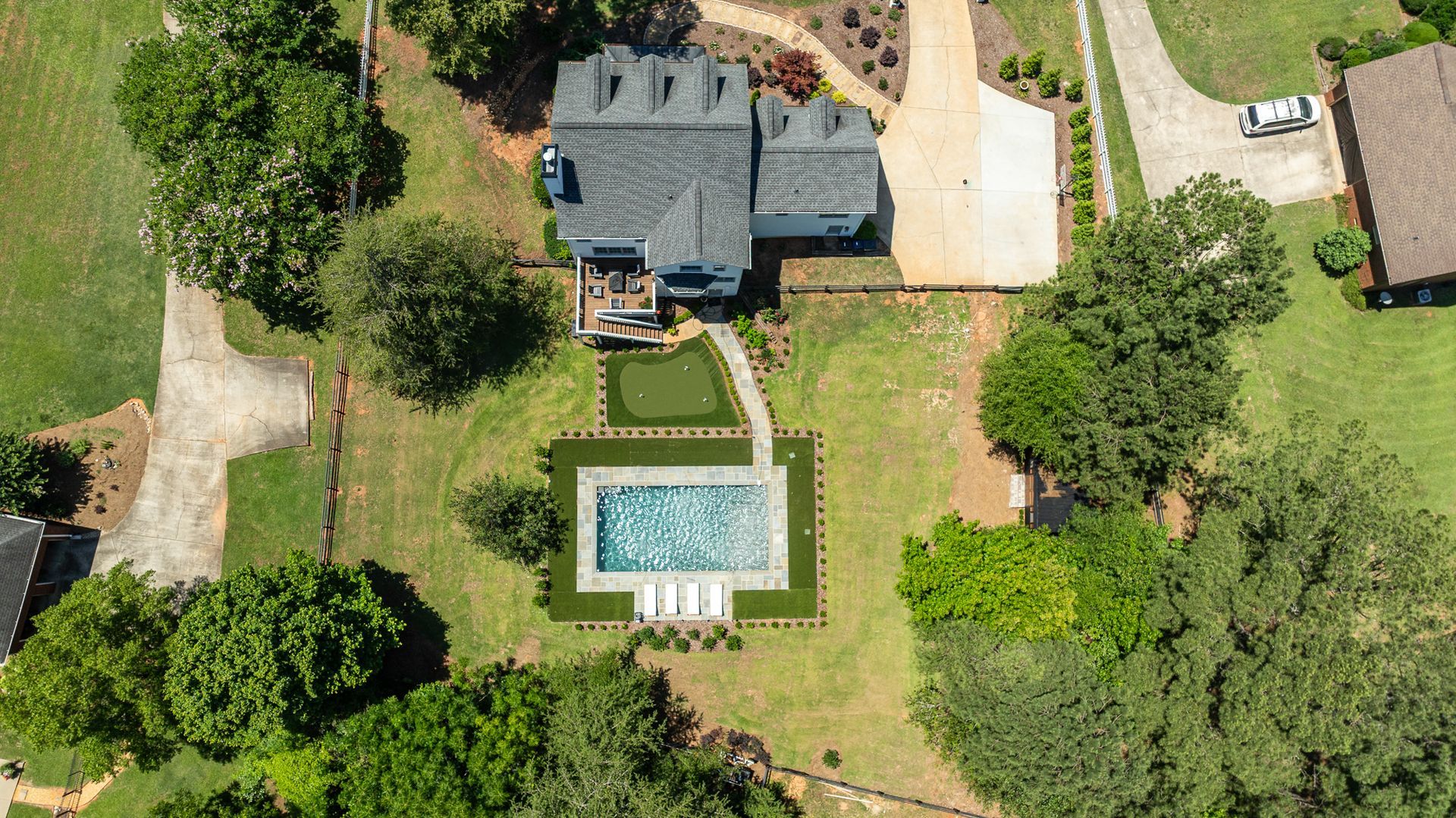 Aerial view of a house, backyard lawn, and rectangular swimming pool surrounded by trees.