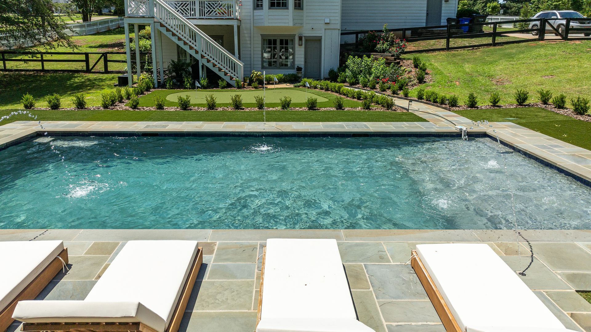 Backyard pool with lounge chairs, stone patio, and house in the background