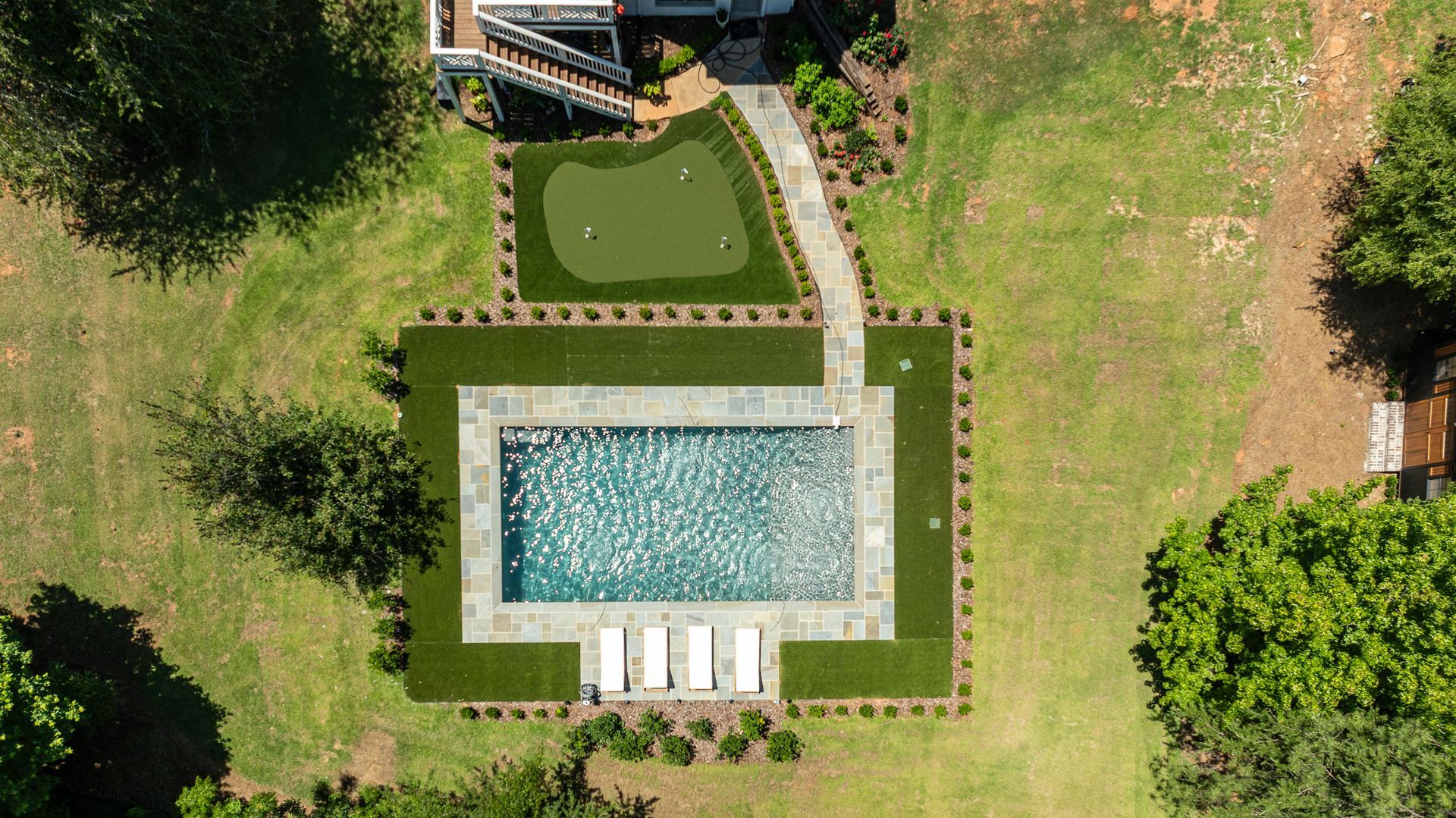 Aerial view of a backyard pool, patio loungers, and green lawn bordered by hedges