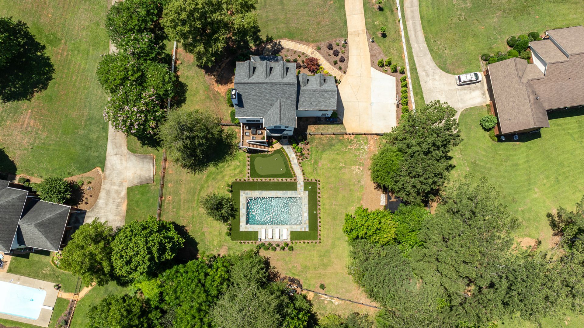 Aerial view of a house with a backyard pool, lawn, trees, and a driveway