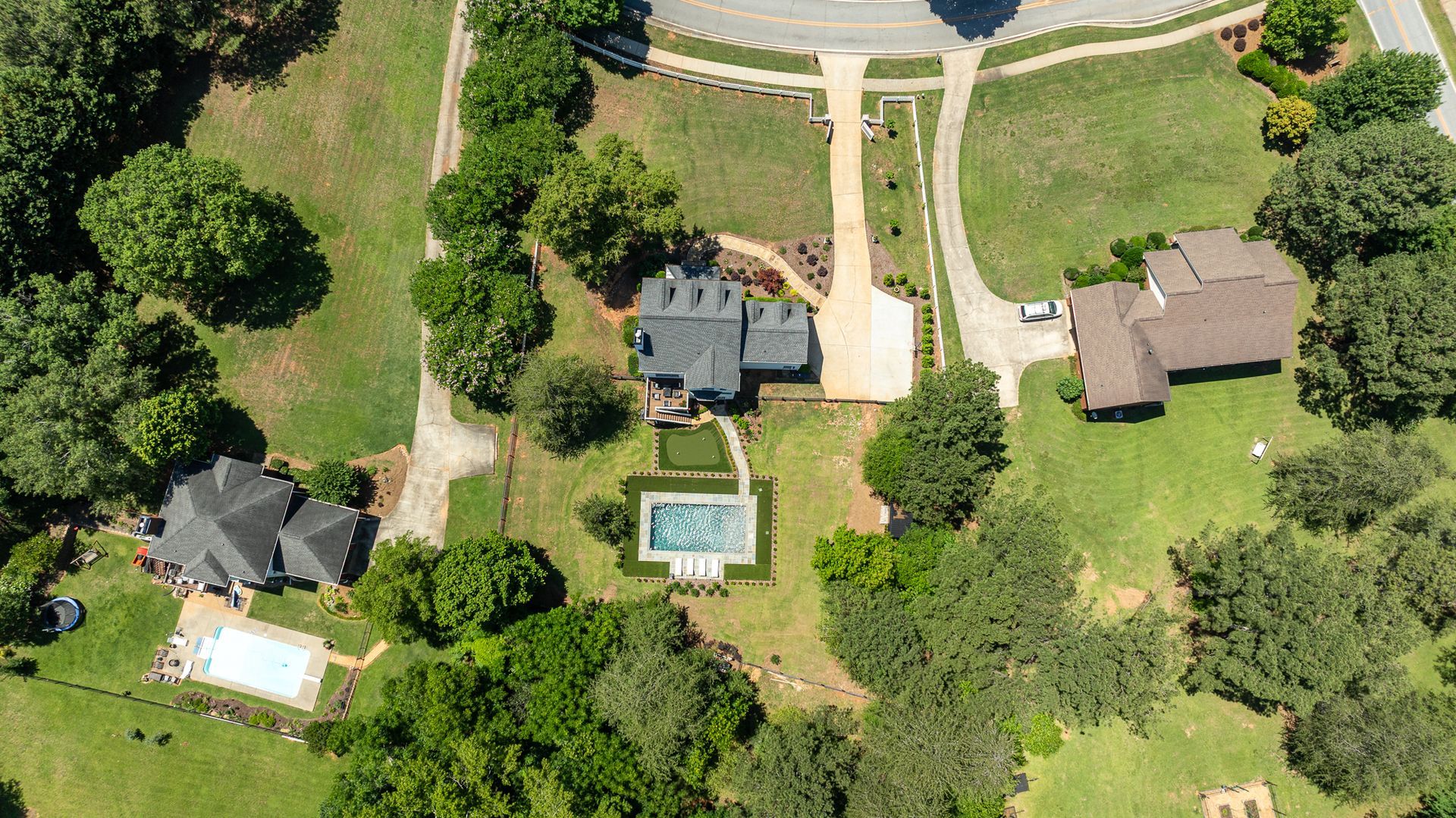 Aerial view of houses, trees, and a swimming pool along a curved road.