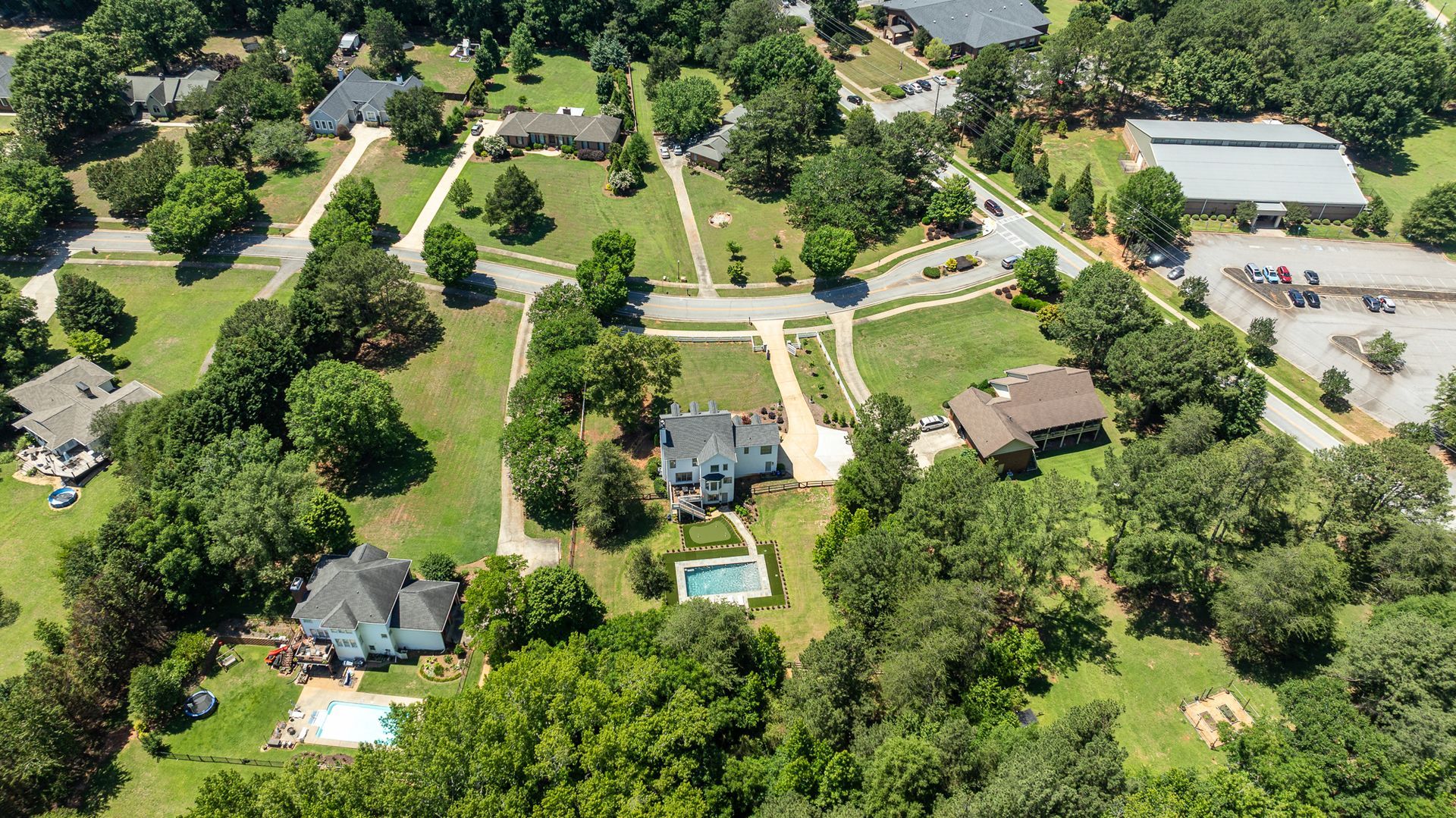 Aerial view of a tree-lined neighborhood with houses, roads, and a swimming pool on a sunny day