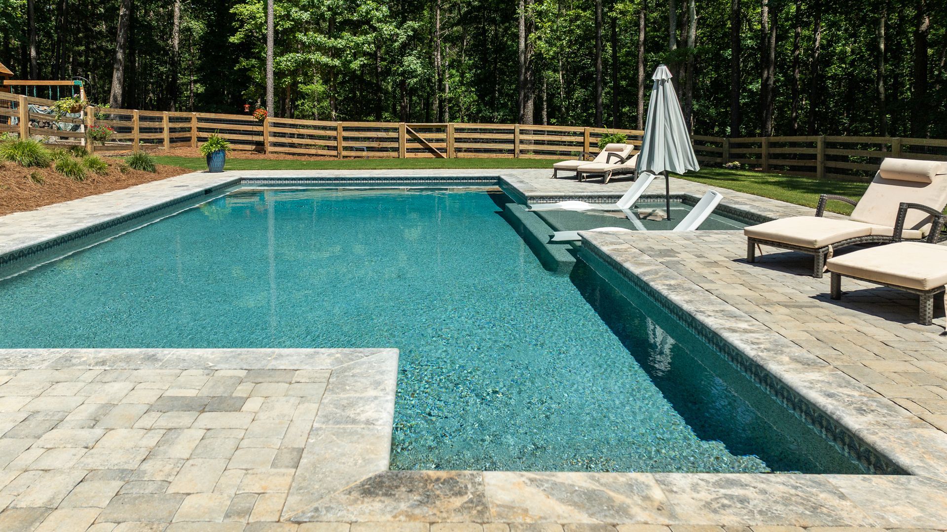 Backyard swimming pool with turquoise water, lounge chairs, and a patio surrounded by trees