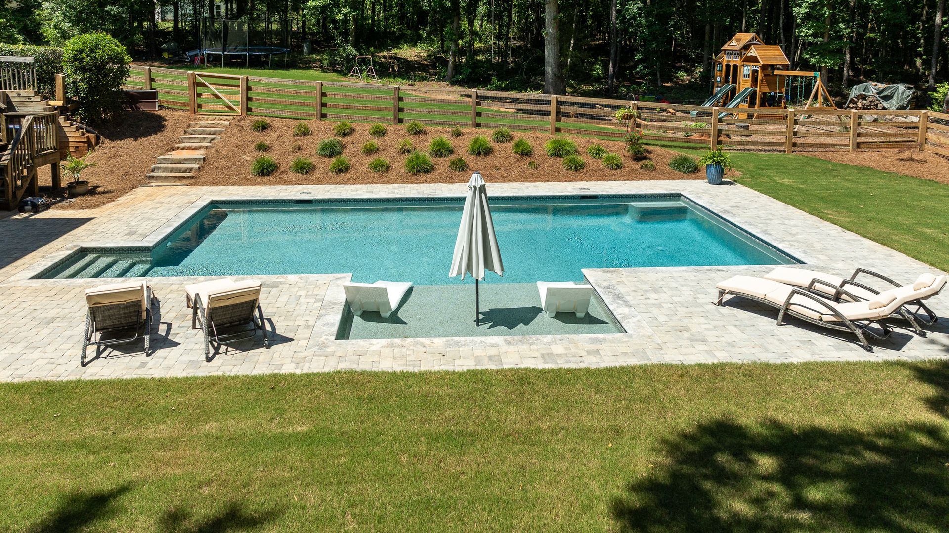 Backyard pool with lounge chairs, patio seating, and landscaped garden in the background
