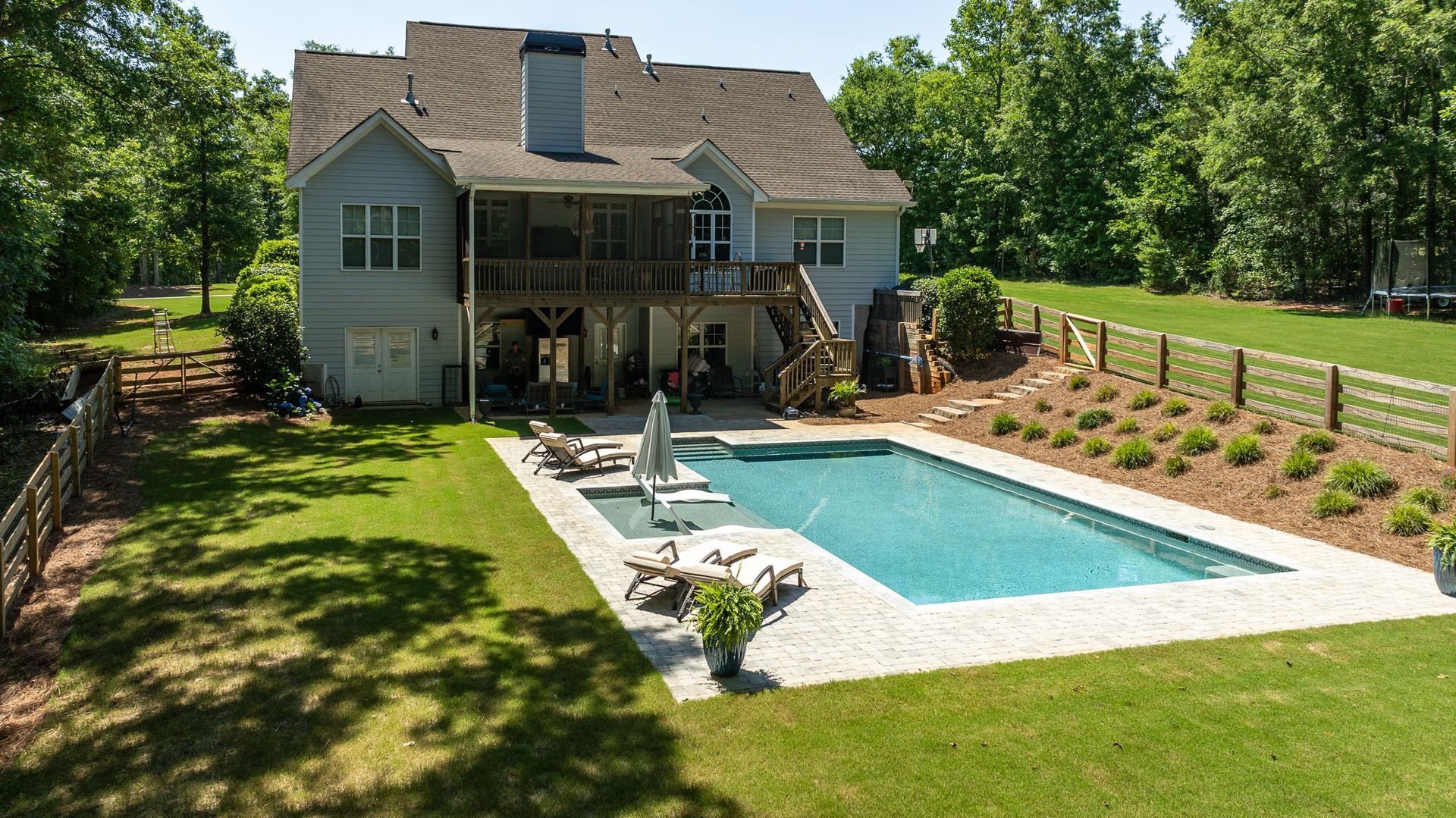 Backyard home with a swimming pool, patio seating, and a fenced lawn surrounded by trees