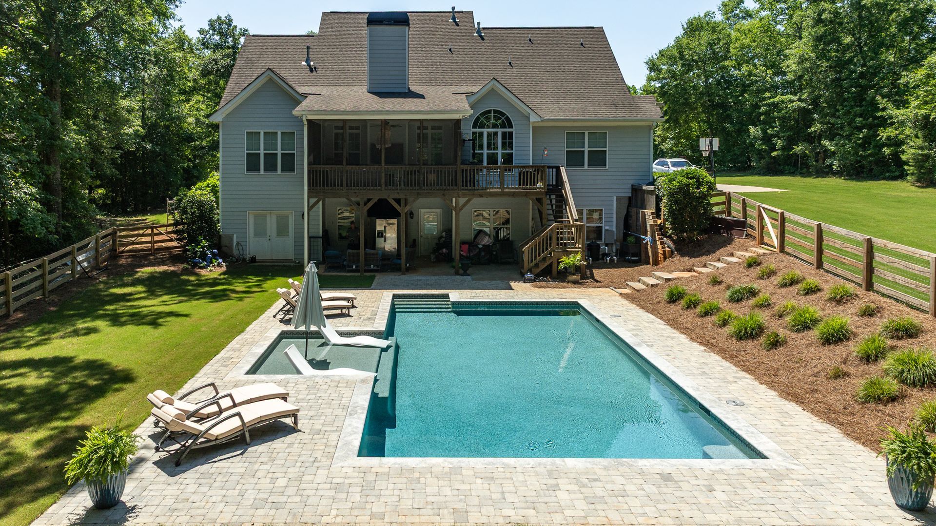 Backyard with a rectangular swimming pool, lounge chairs, and a two-story house with a patio.