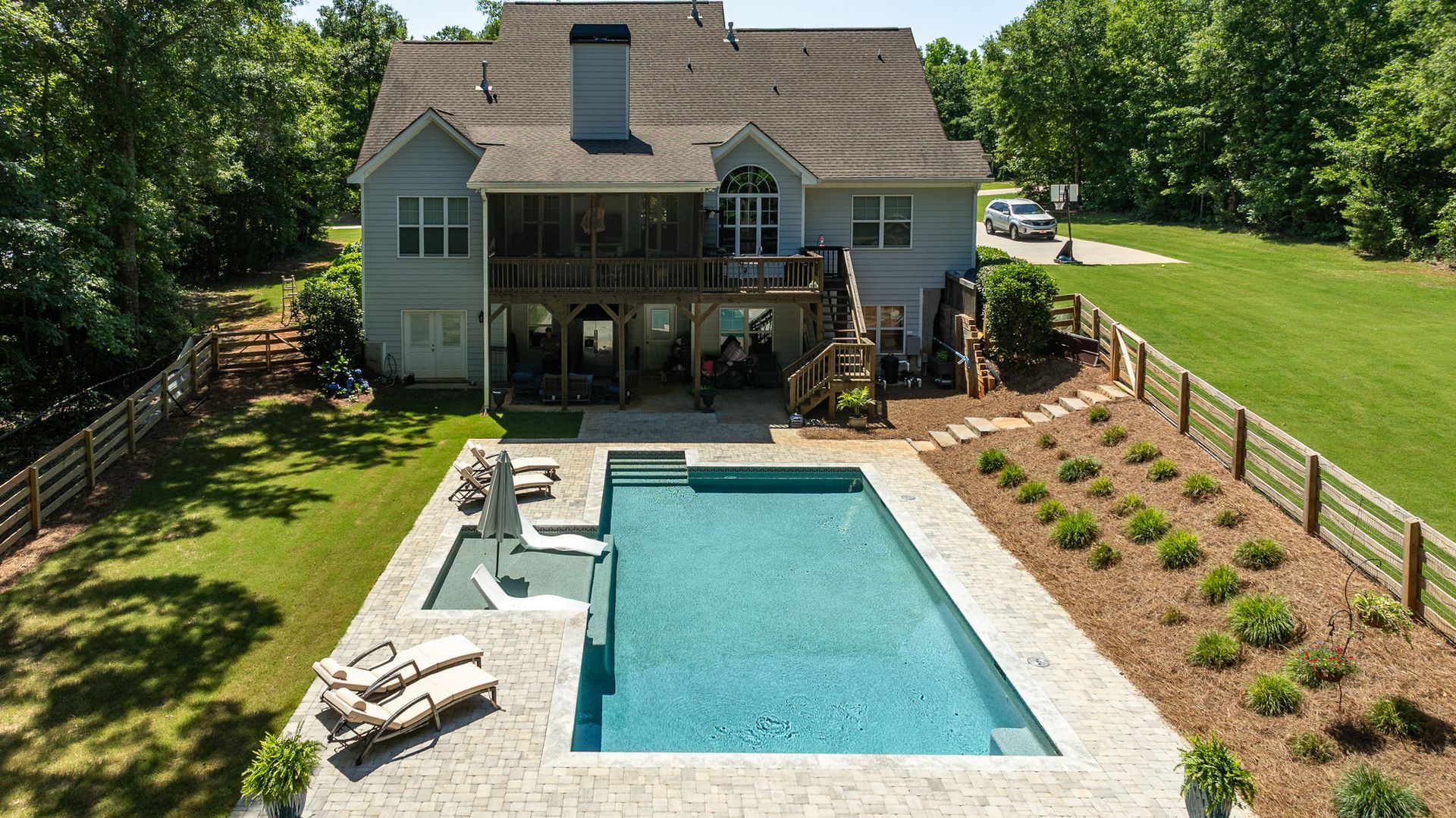 Backyard with a rectangular pool, lounge chairs, patio, and a house surrounded by green lawn and trees