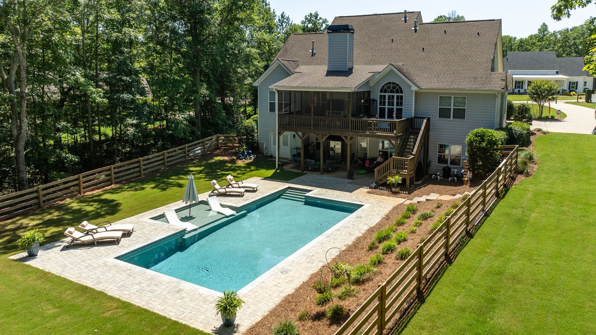 Backyard with a rectangular swimming pool, patio seating, and a two-story house surrounded by a wooden fence.
