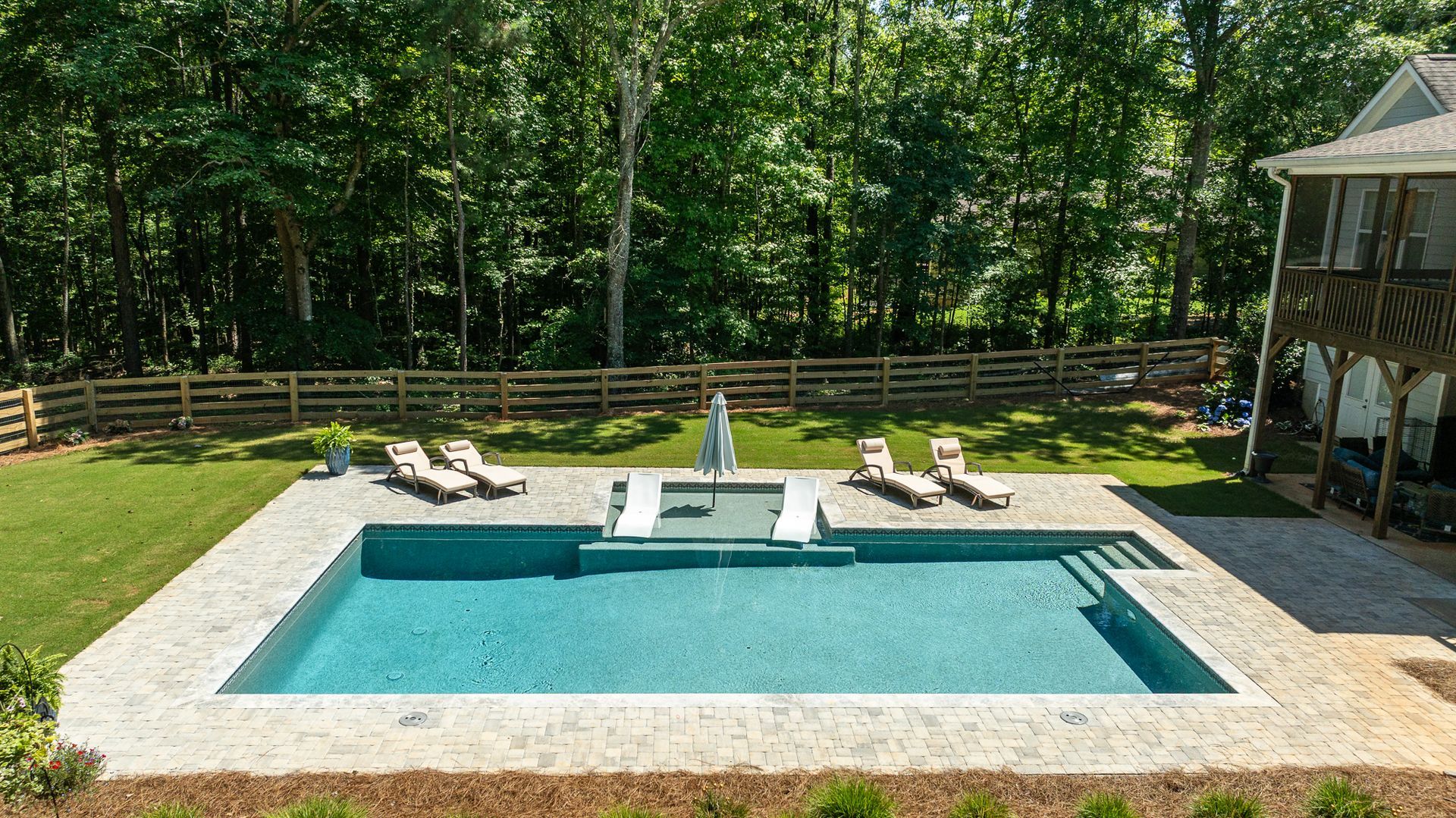 Backyard pool with lounge chairs, a diving board, and a deck surrounded by trees
