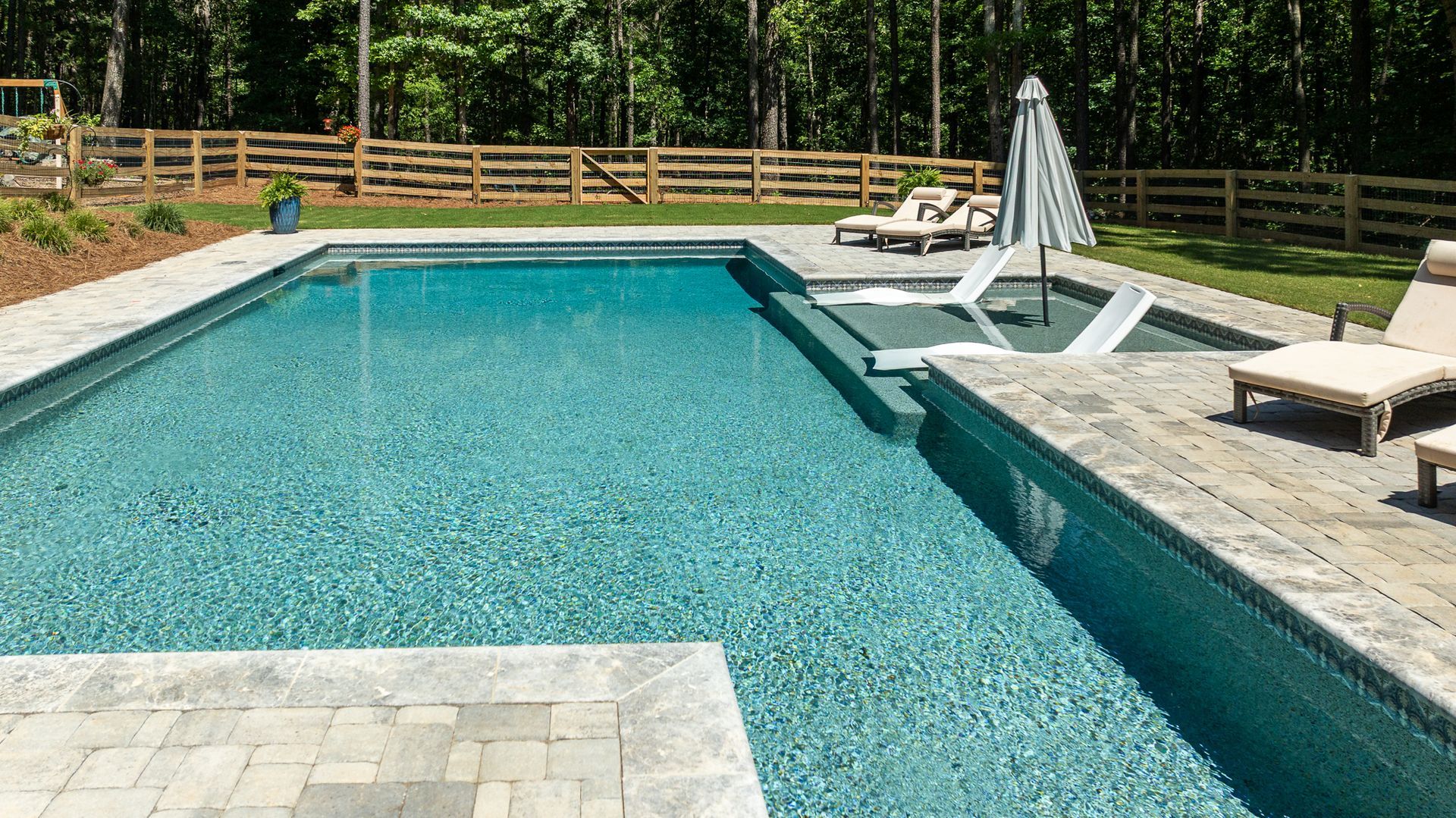 Rectangular backyard swimming pool with lounge chairs, a patio, and a wooden fence