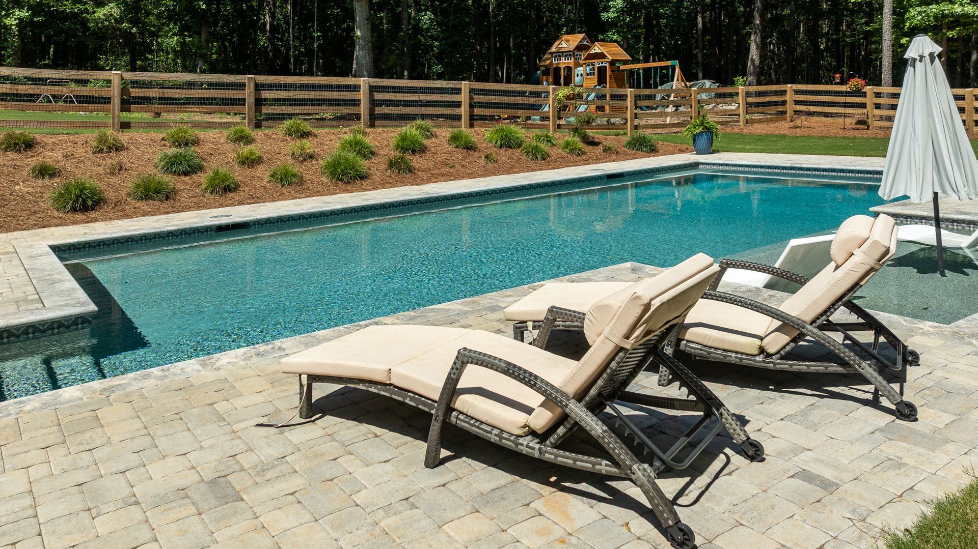 Backyard swimming pool with two lounge chairs and an umbrella on a stone patio