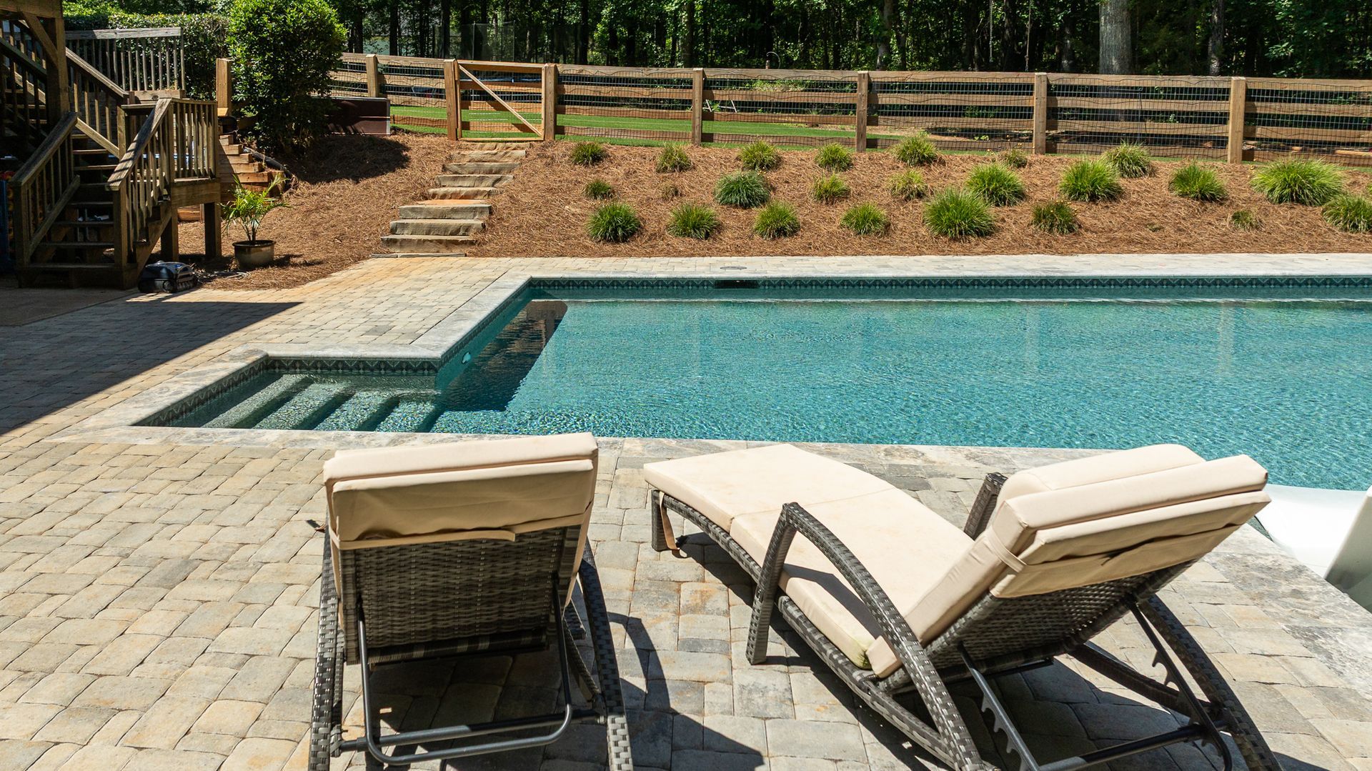 Backyard pool with lounge chairs, paver patio, and landscaped fence line under bright sun