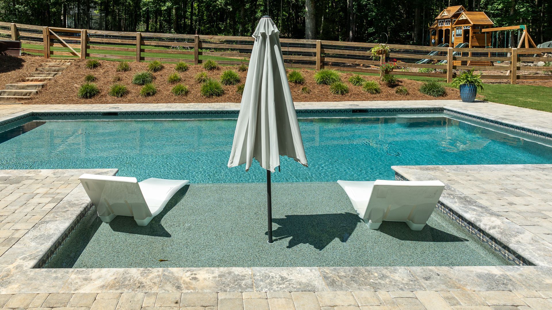 Poolside lounge chairs and umbrella on a stone platform beside a swimming pool.