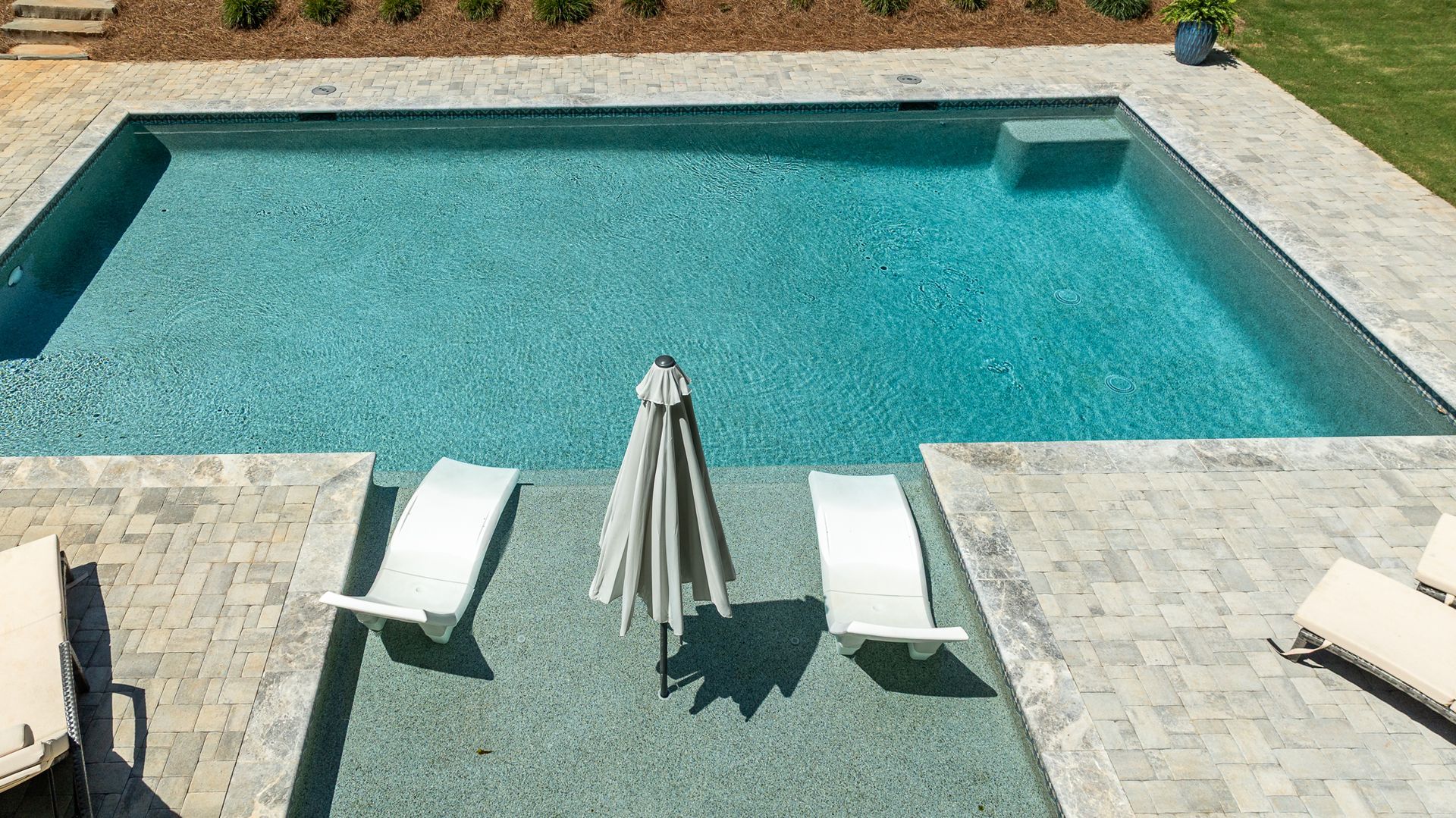 Outdoor swimming pool with turquoise water, white lounge chairs, and a closed umbrella on the patio.