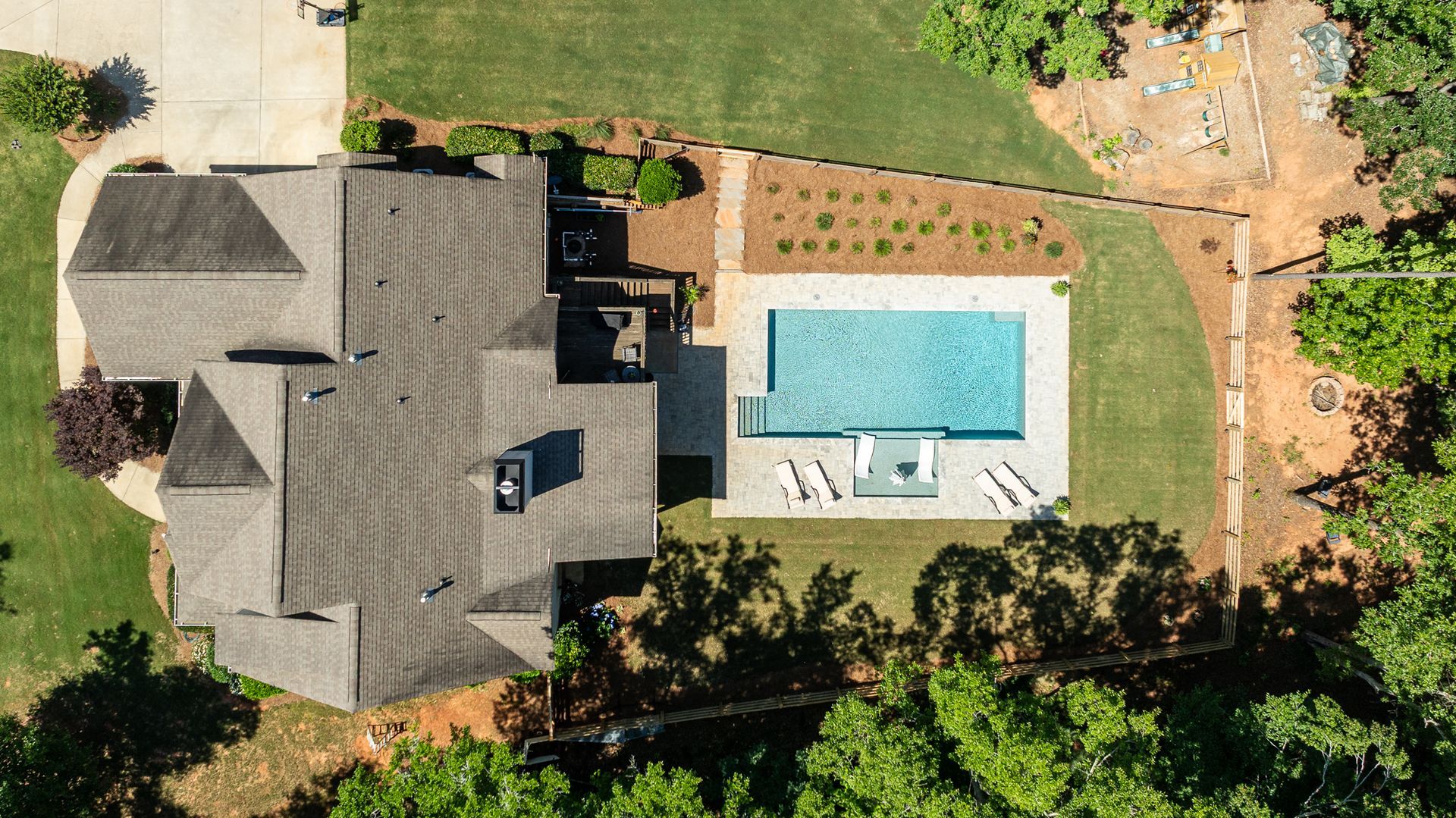 Aerial view of a house with a backyard pool, patio loungers, and a manicured lawn.