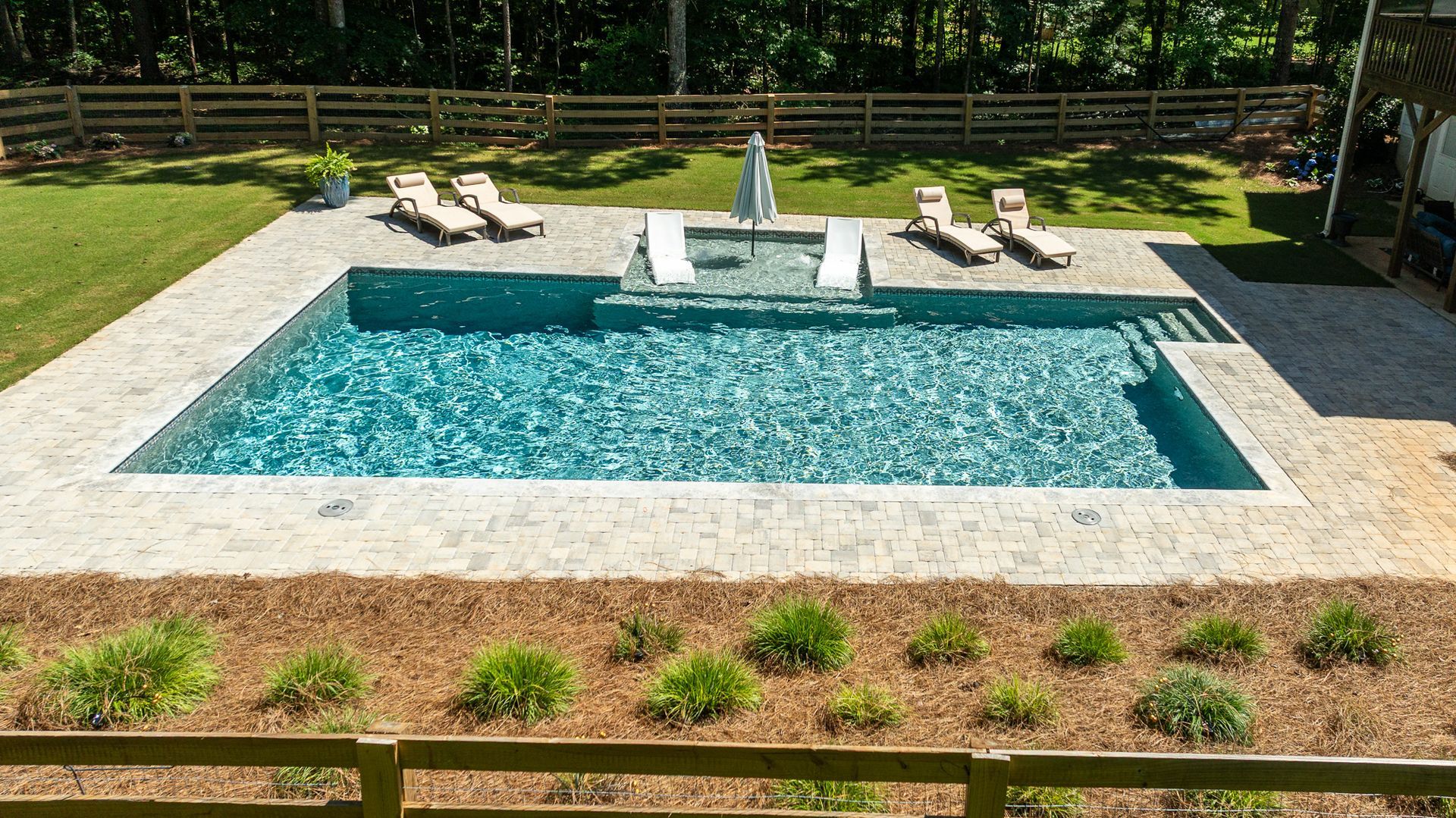 Backyard swimming pool with lounge chairs, white steps, and green lawn fencing.
