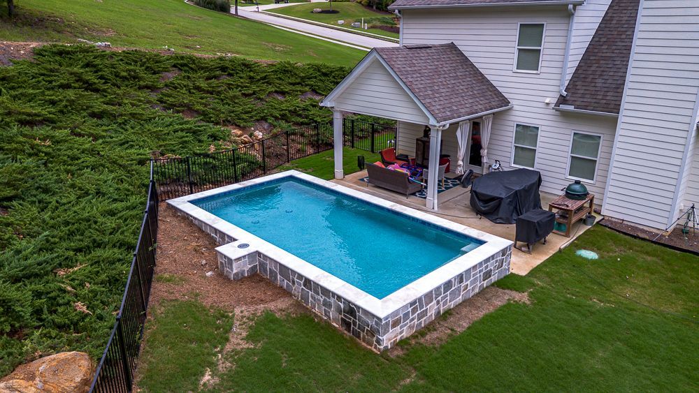 Backyard with rectangular pool, white house, patio furniture, and green lawn.
