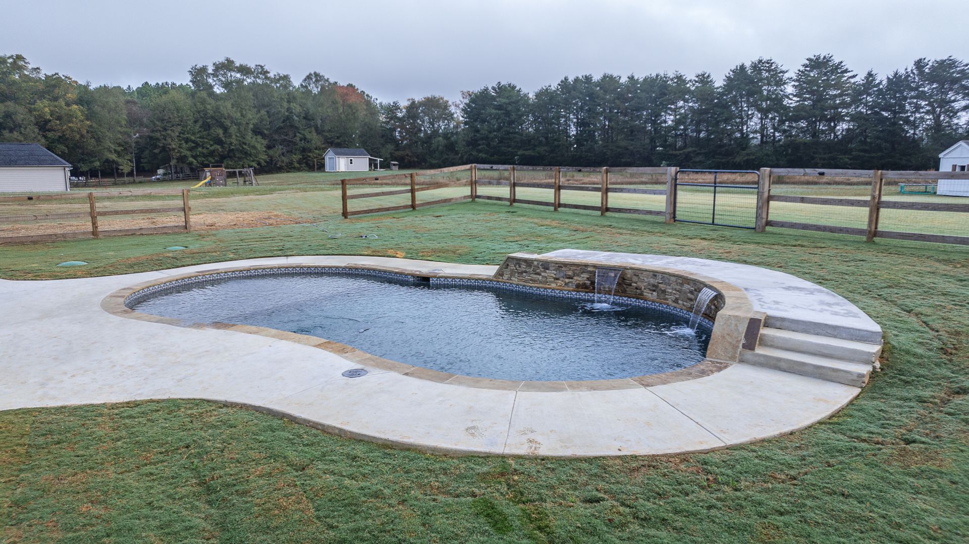 A large swimming pool is in the middle of a lush green field.