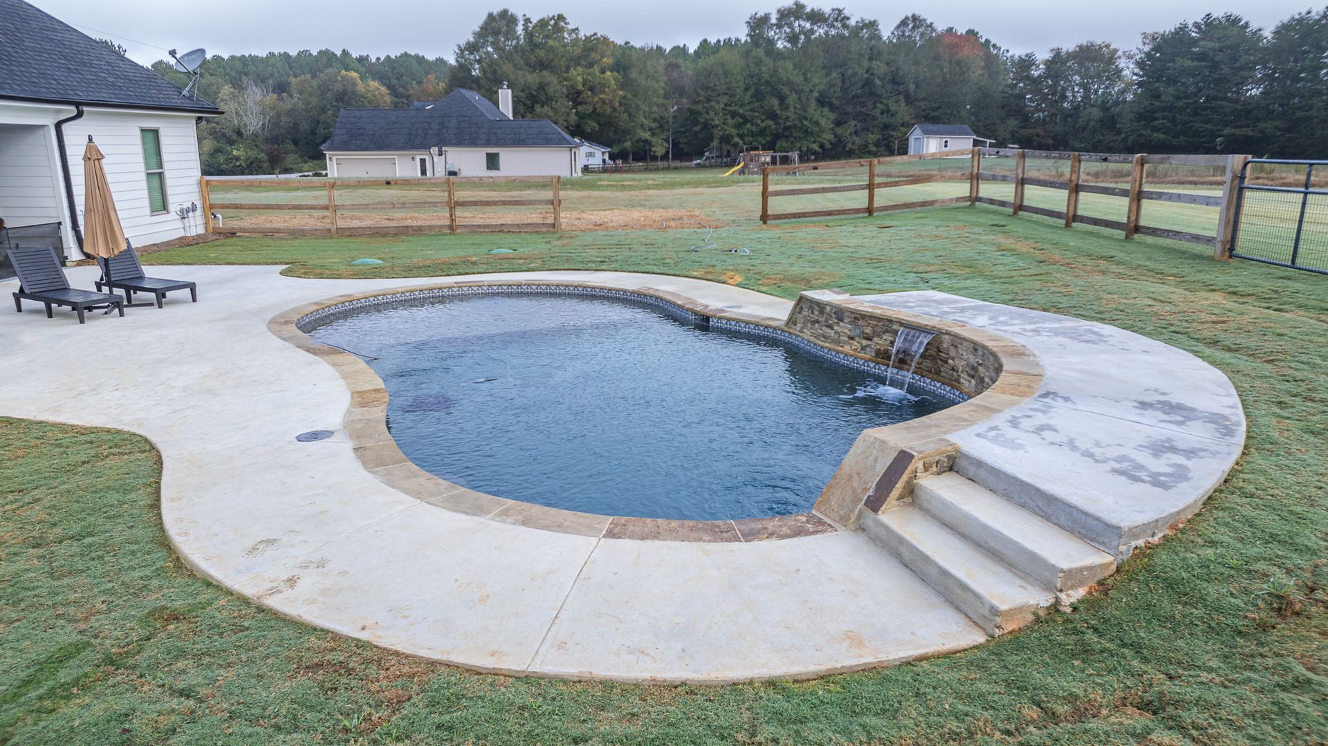 A large swimming pool is in the backyard of a house.