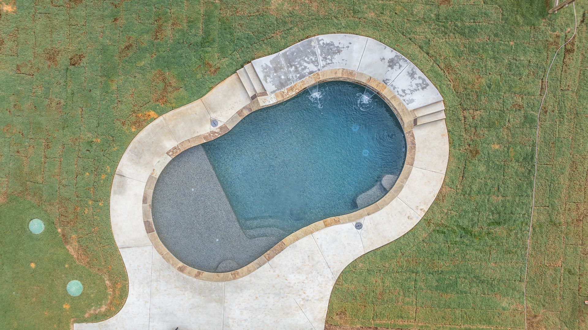 An aerial view of a large swimming pool in the middle of a lush green field.