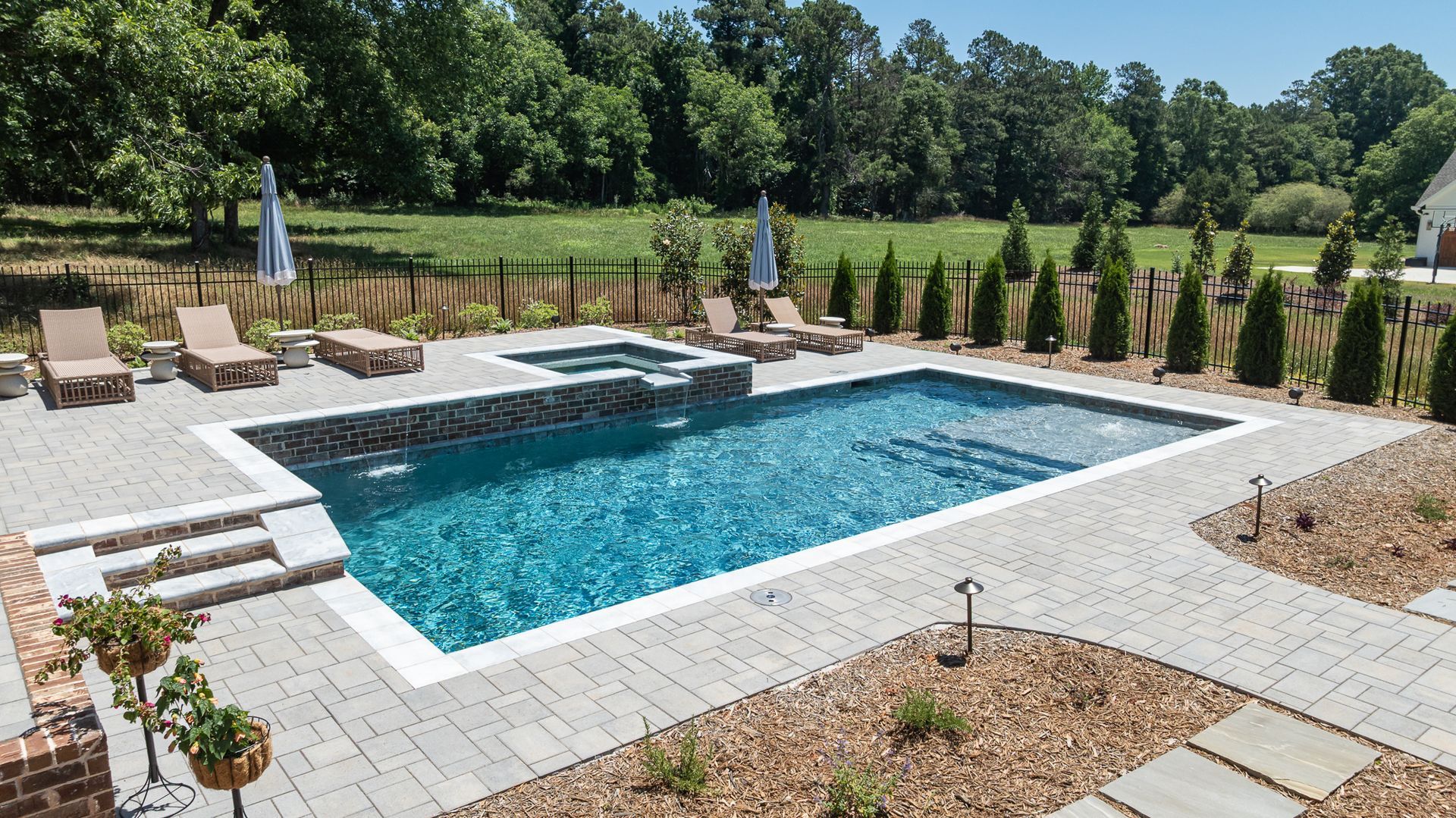 Backyard swimming pool with lounge chairs, umbrellas, and landscaped greenery
