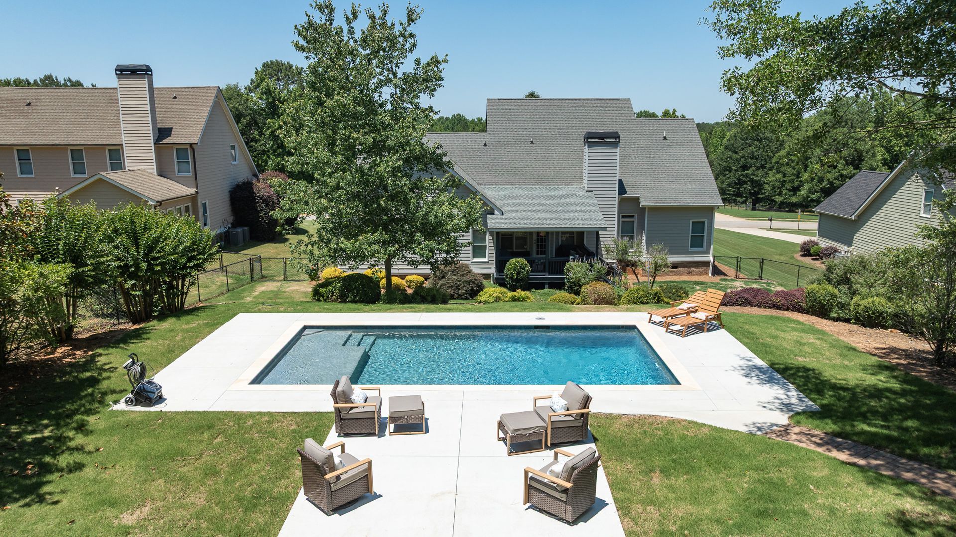 Backyard with rectangular pool, white patio, and wicker seating beside a house