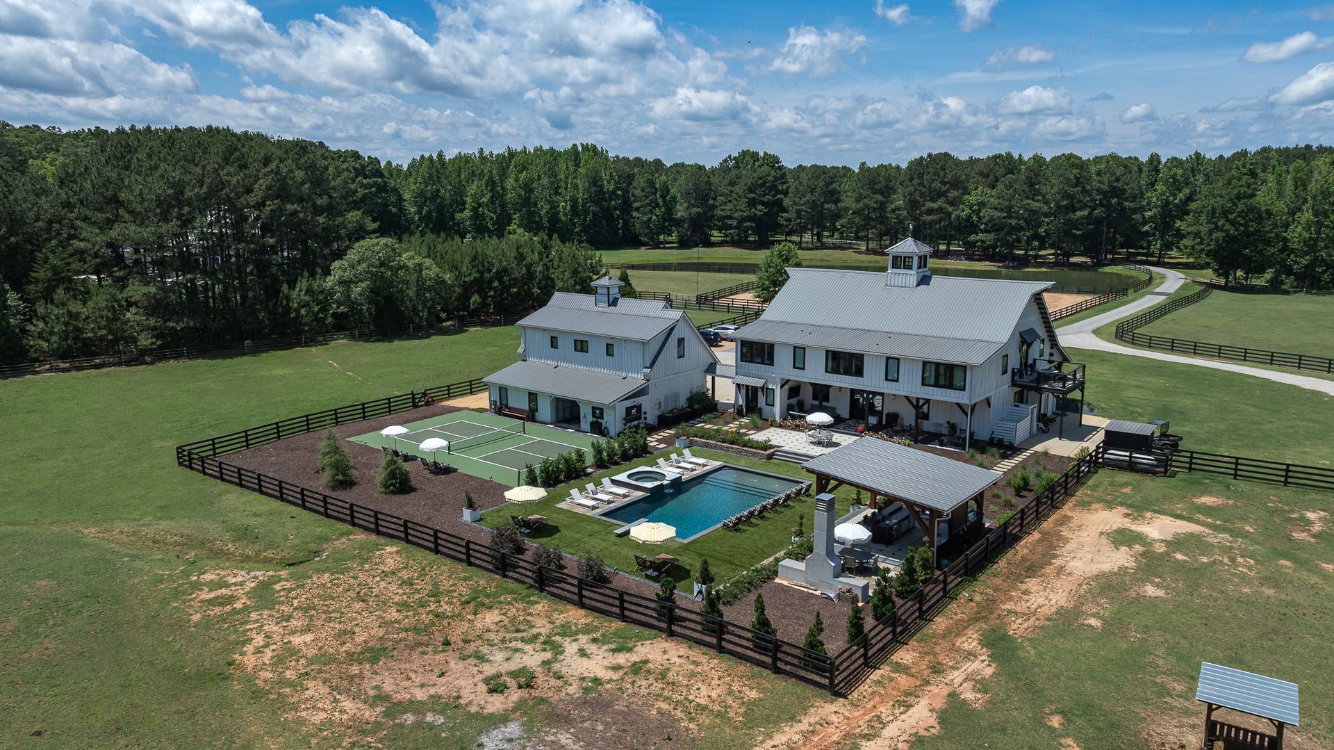 Aerial view of a white house with a fenced backyard, pool, and patio on a grassy rural property