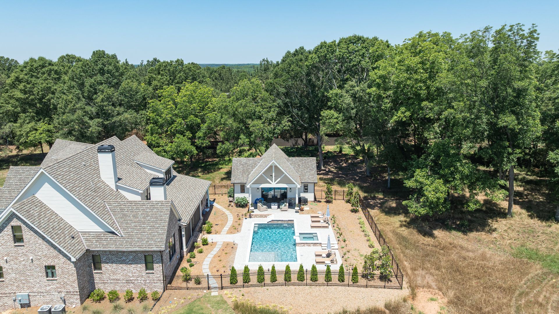 Aerial view of a stone house with a backyard pool, patio, and surrounding trees in a wooded setting