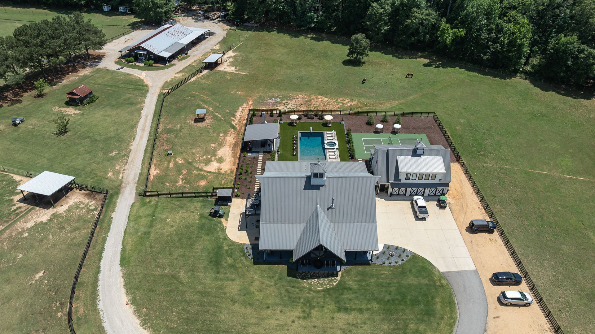 Aerial view of a house with a swimming pool, driveway, and surrounding green lawn and trees