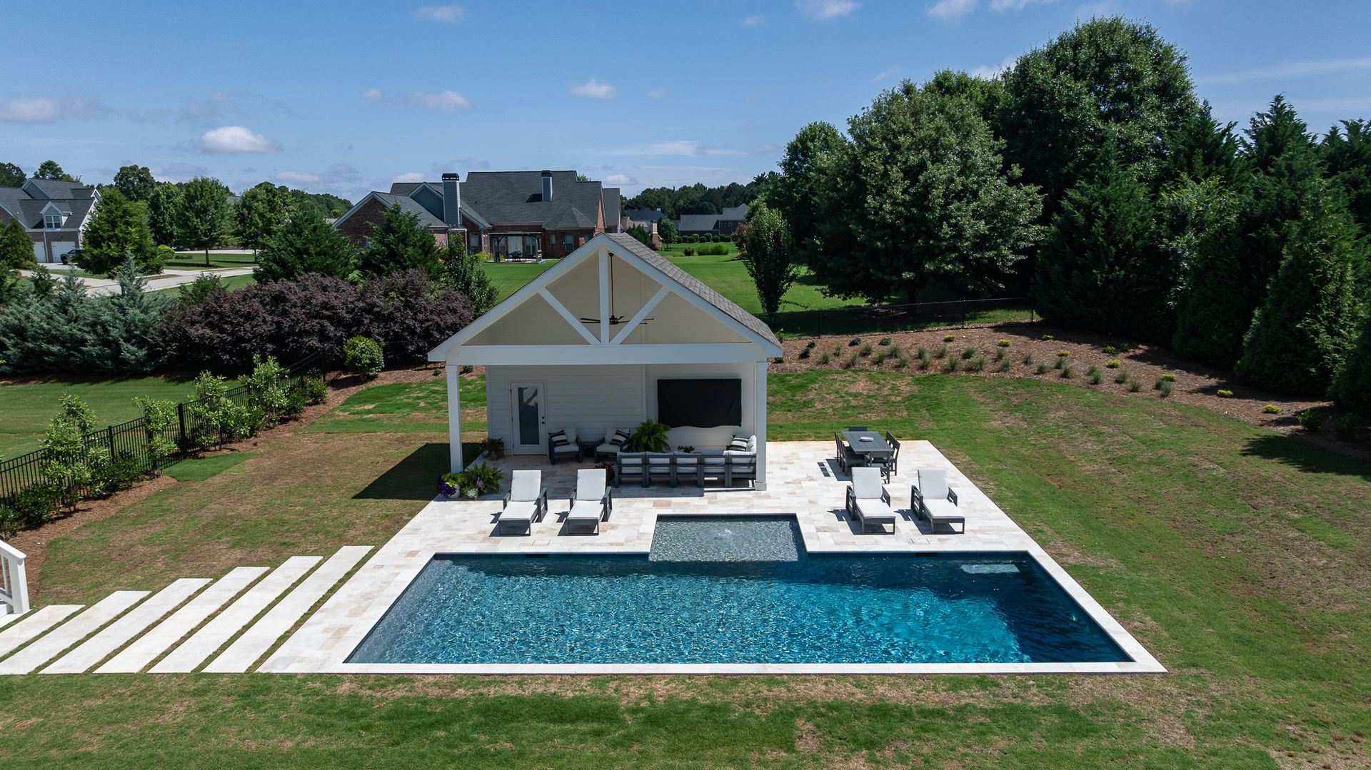 Modern white house with a patio and blue swimming pool in a sunny garden