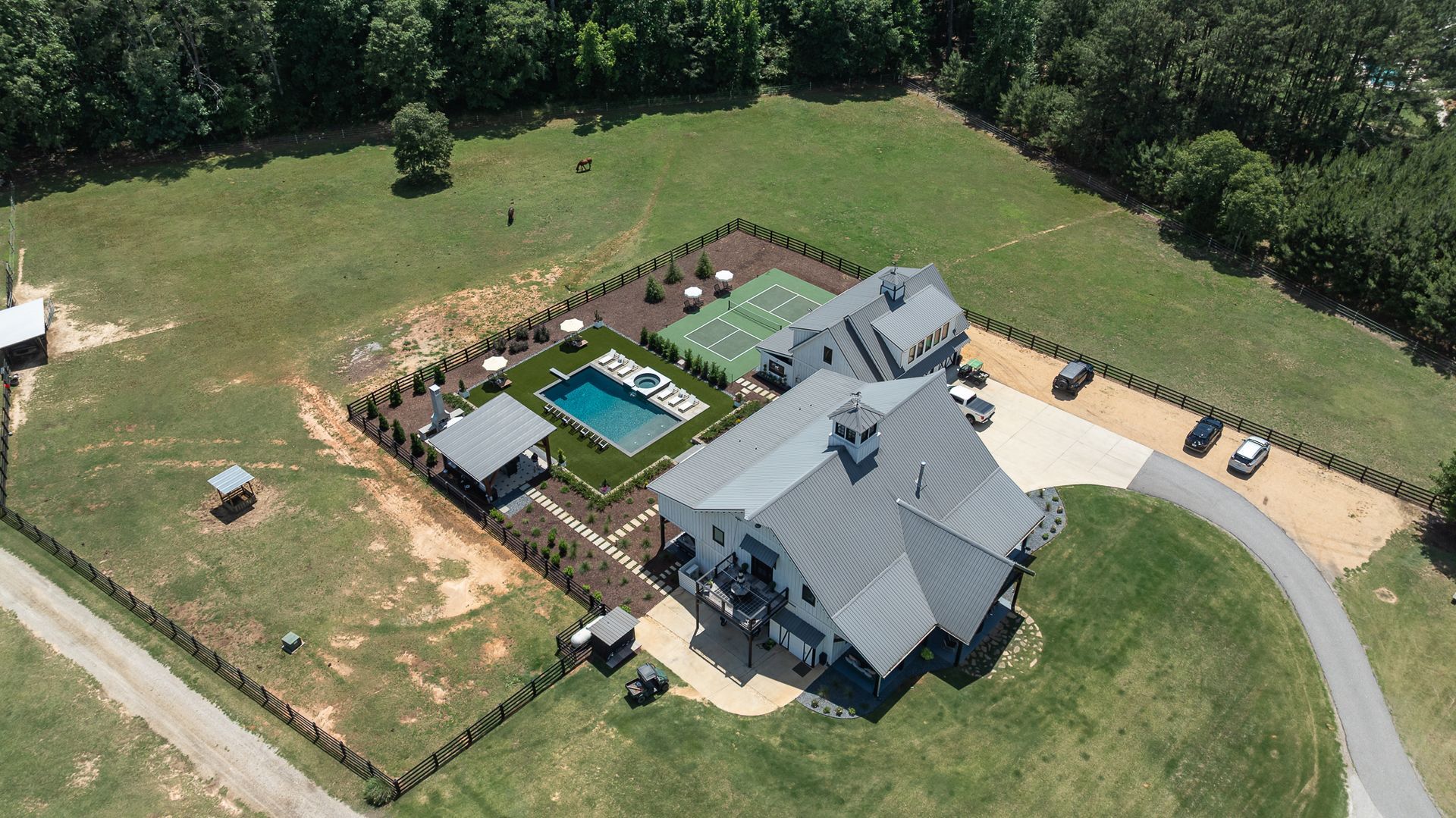 Aerial view of a large gray house with a pool, patio, and lawn surrounded by trees.