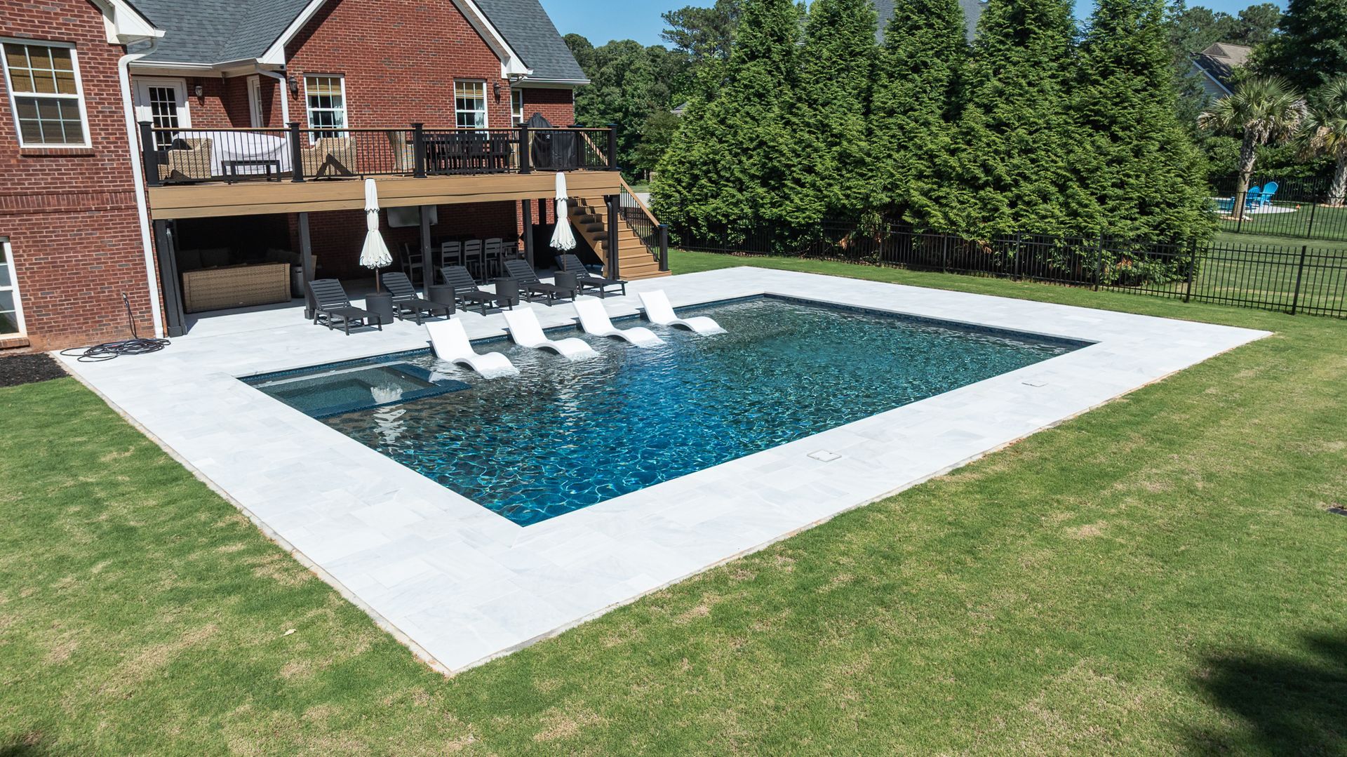 Backyard pool with lounge chairs beside a brick house and green lawn