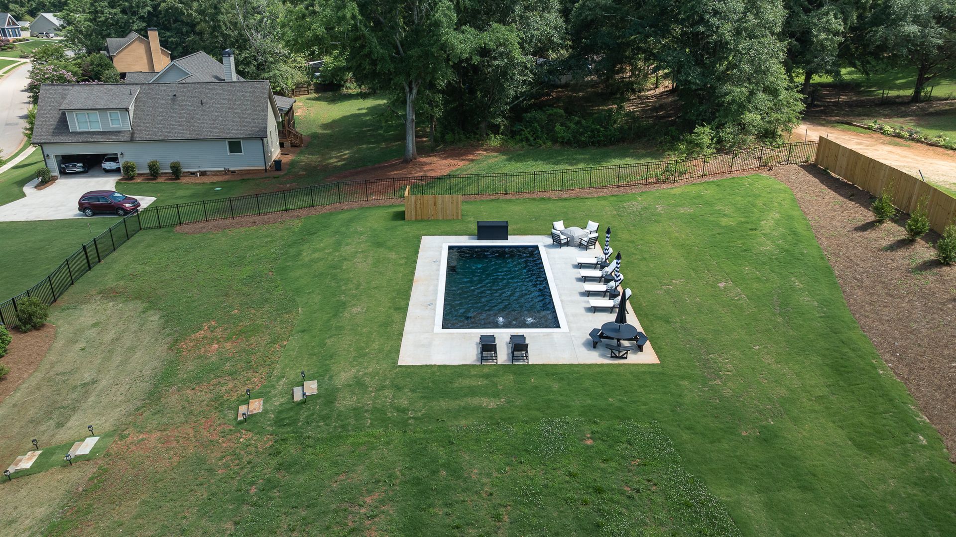 Aerial view of a backyard with a rectangular swimming pool, lounge chairs, lawn, and a house nearby