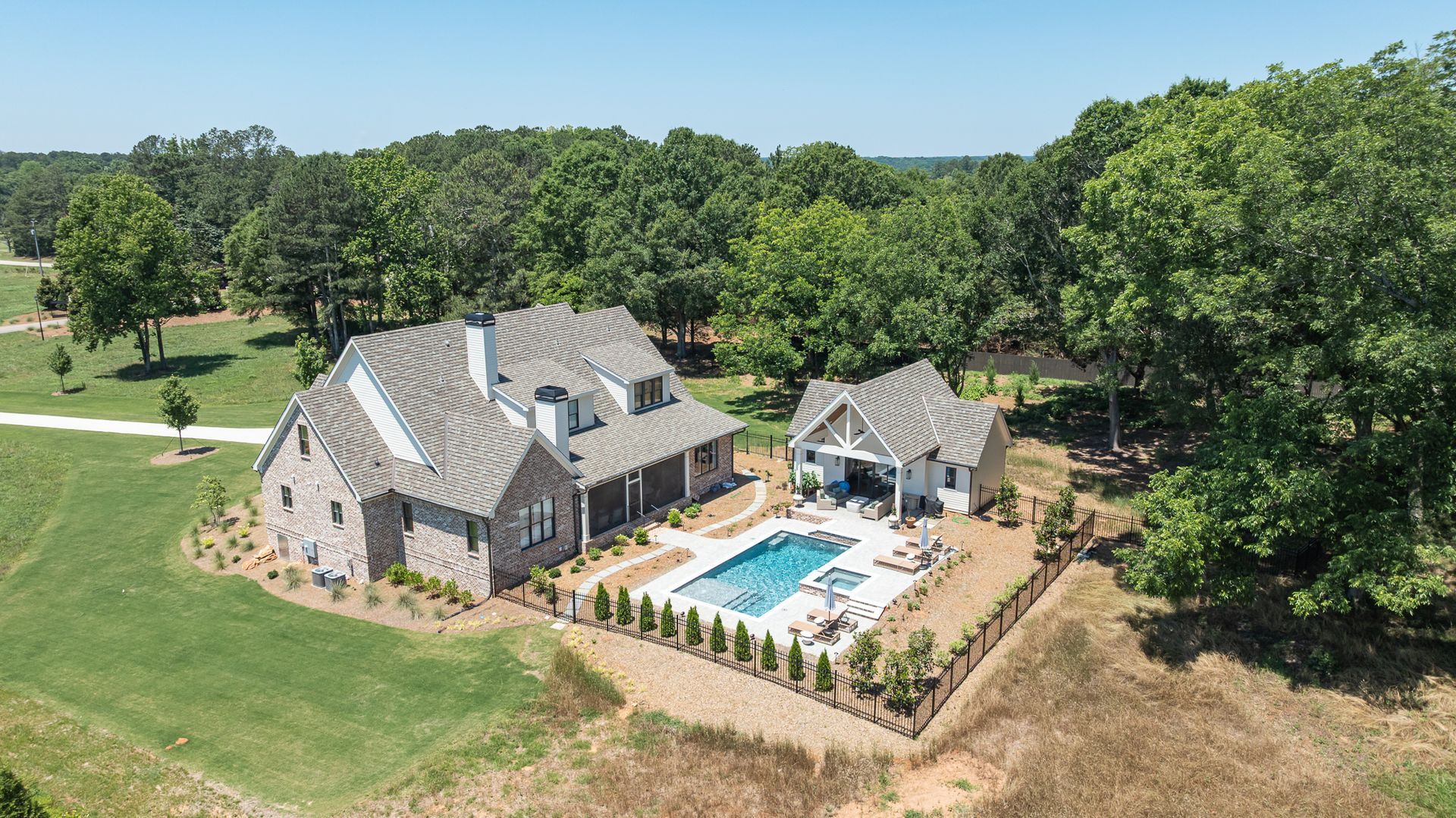 Aerial view of a large stone house with a pool, patio, and trees surrounding the property.