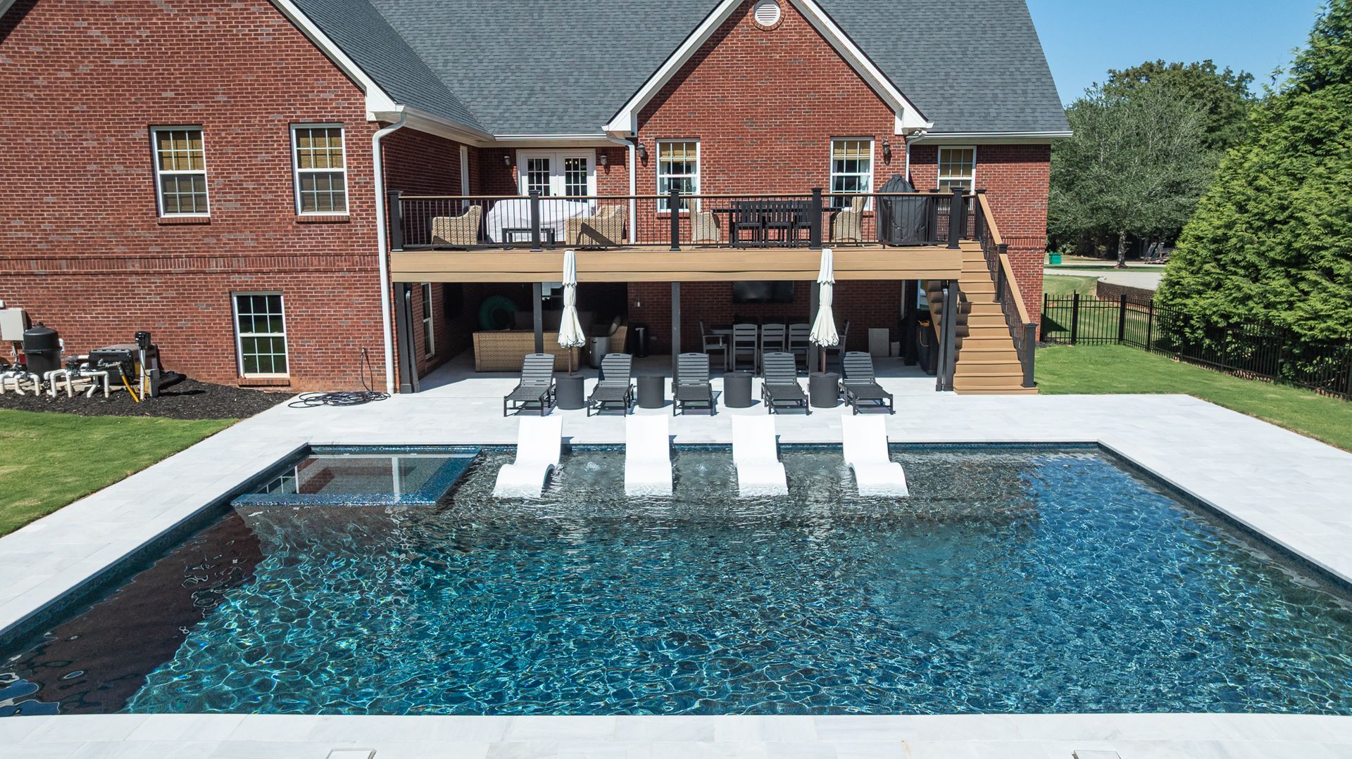 Backyard with a swimming pool, white lounge chairs, and a red brick house with a deck.