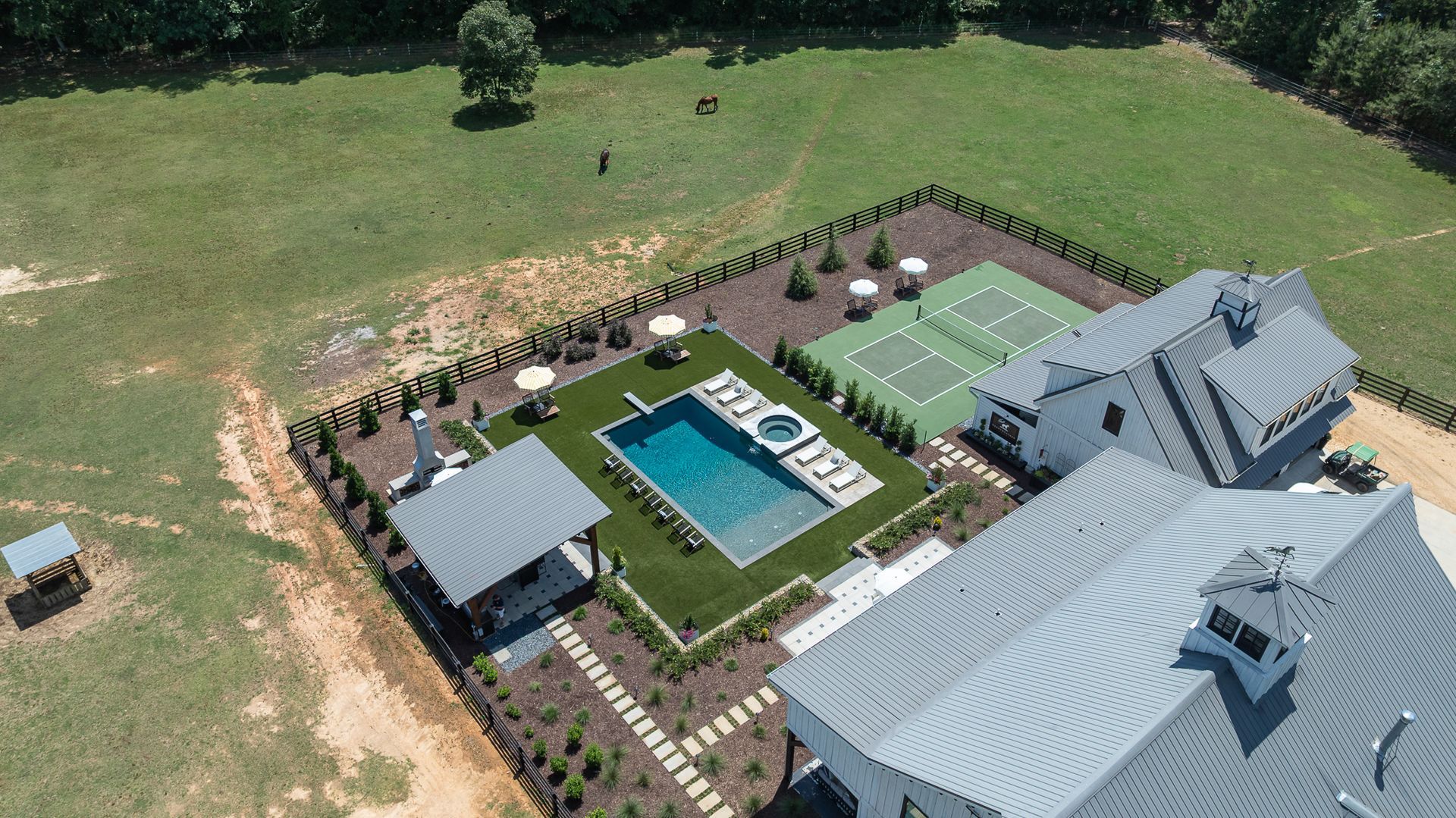 Aerial view of a house with a pool, patio, and fenced yard beside open grassy land
