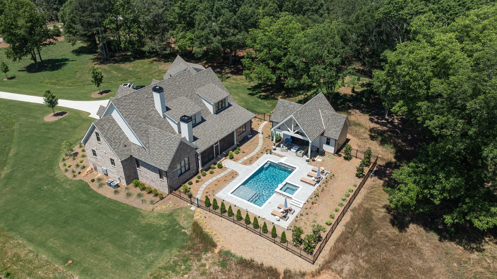 Aerial view of a large gray house with a fenced backyard, pool, patio, and surrounding trees.