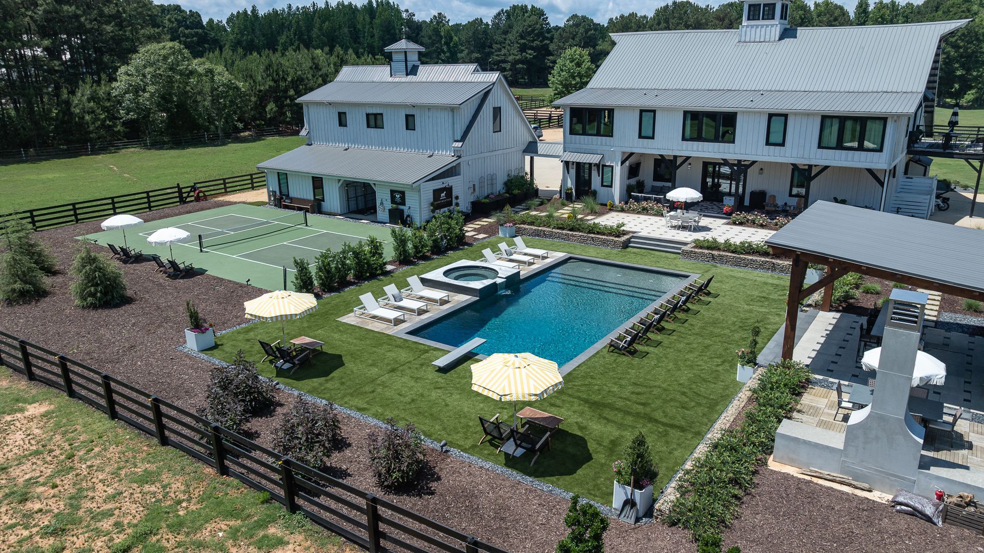 Aerial view of a farmhouse with a swimming pool, patio, and landscaped yard surrounded by fencing.