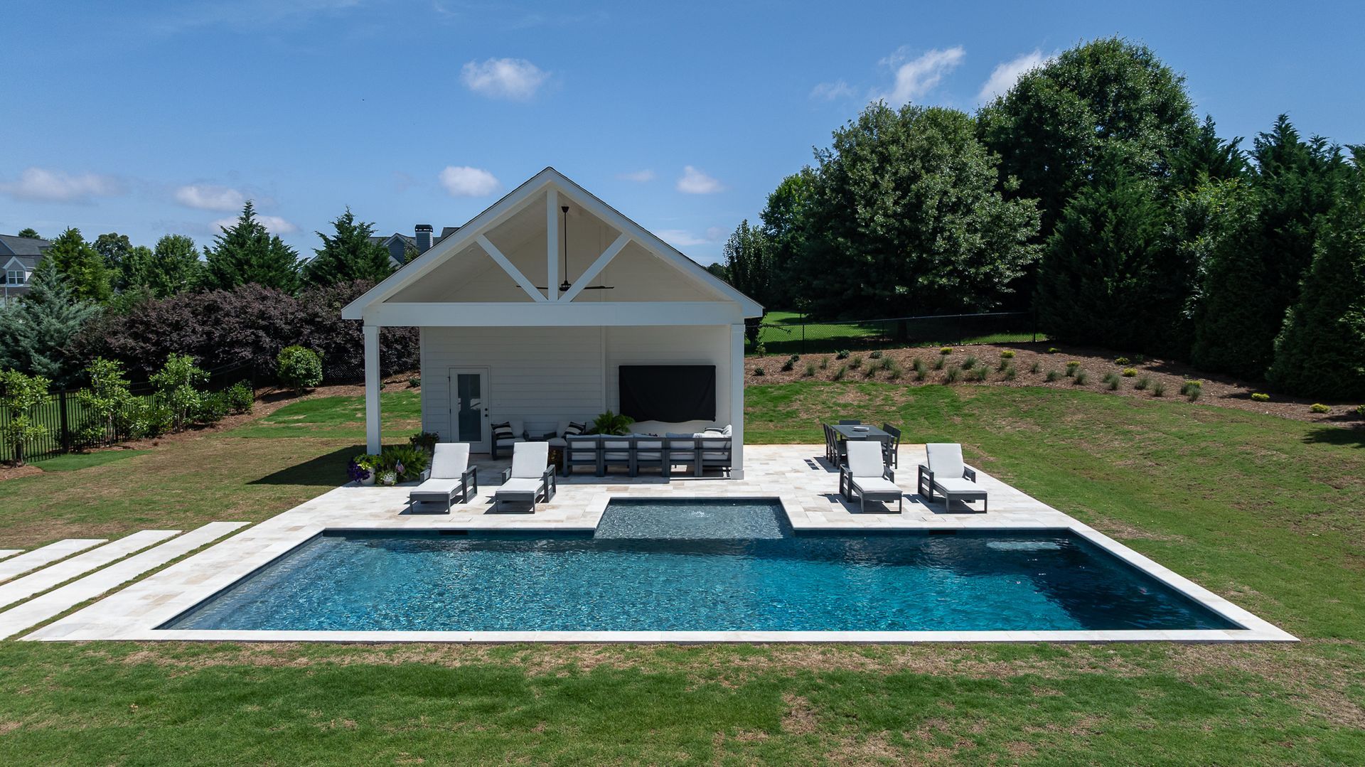 Modern white house with a pool, lounge chairs, and manicured green lawn under a blue sky