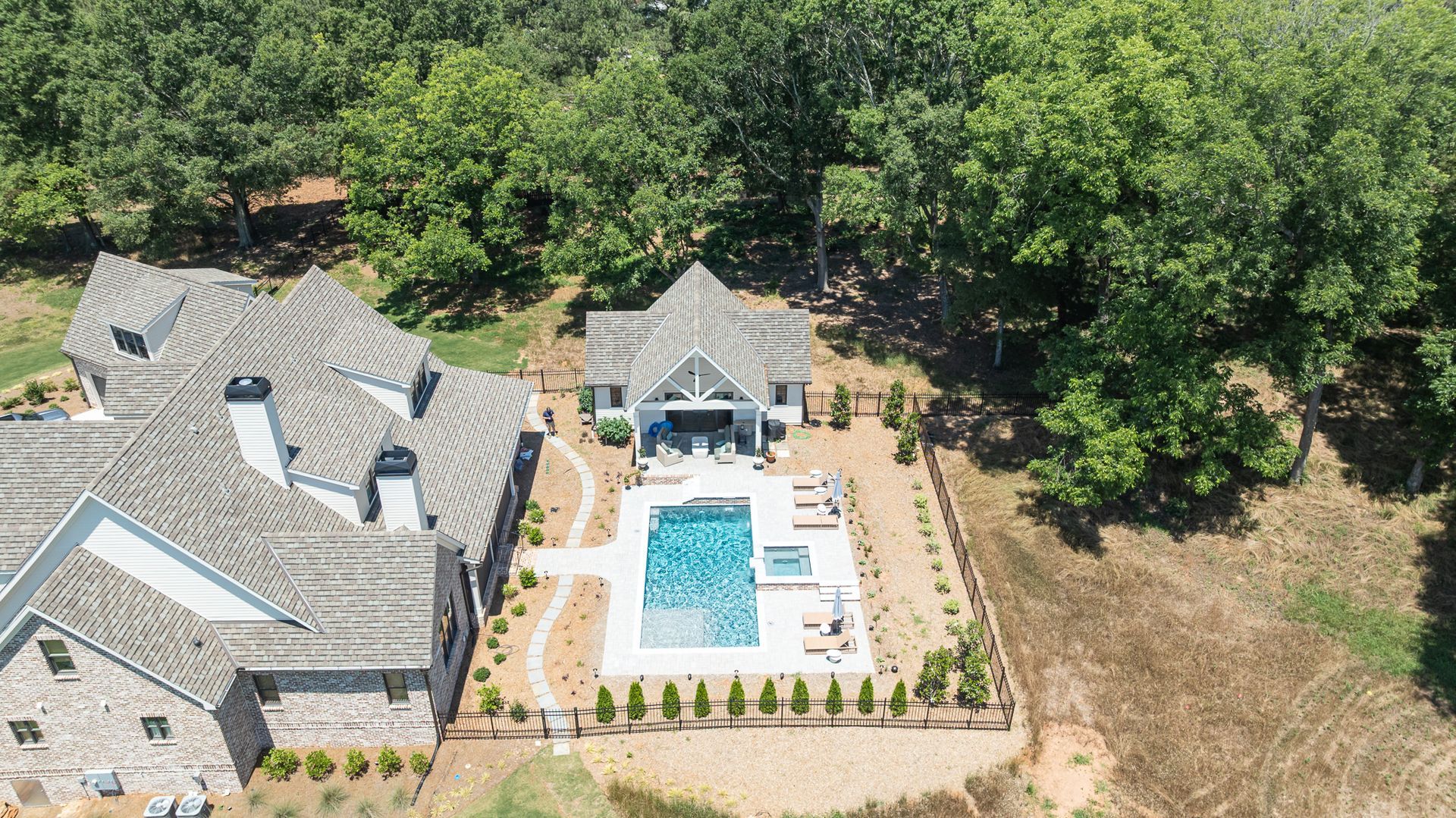 Aerial view of a large house with a fenced pool and patio, surrounded by trees and a lawn.