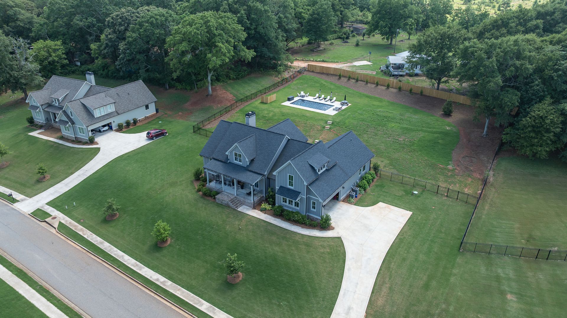 Aerial view of two large houses with driveways, lawns, and a backyard swimming pool in a wooded suburban area