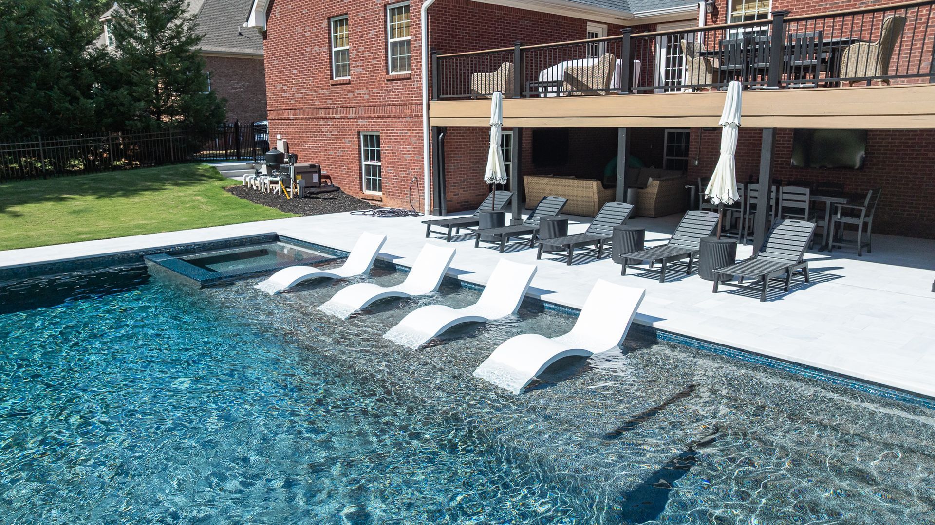 Backyard pool with white loungers and umbrellas beside a brick house