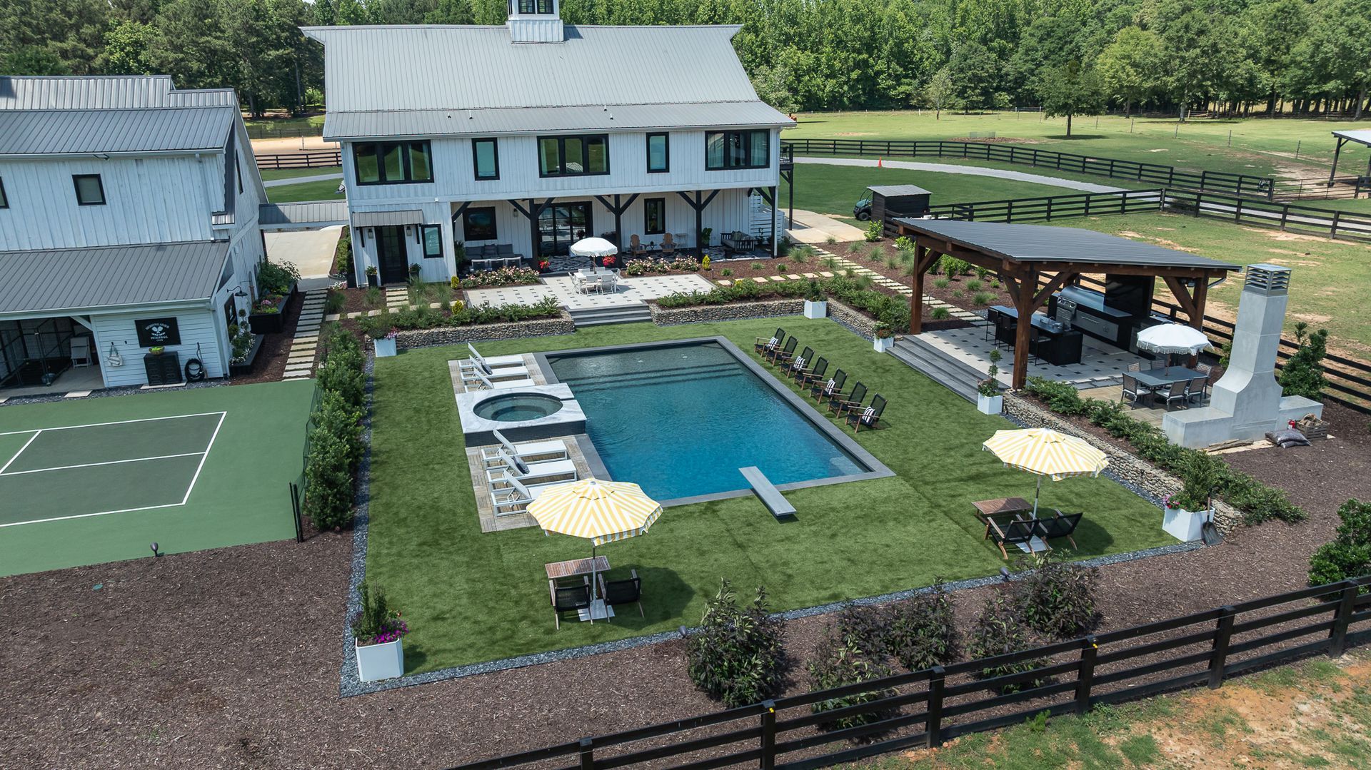 Aerial view of a house with a backyard pool, patio, and fenced lawn on a sunny day