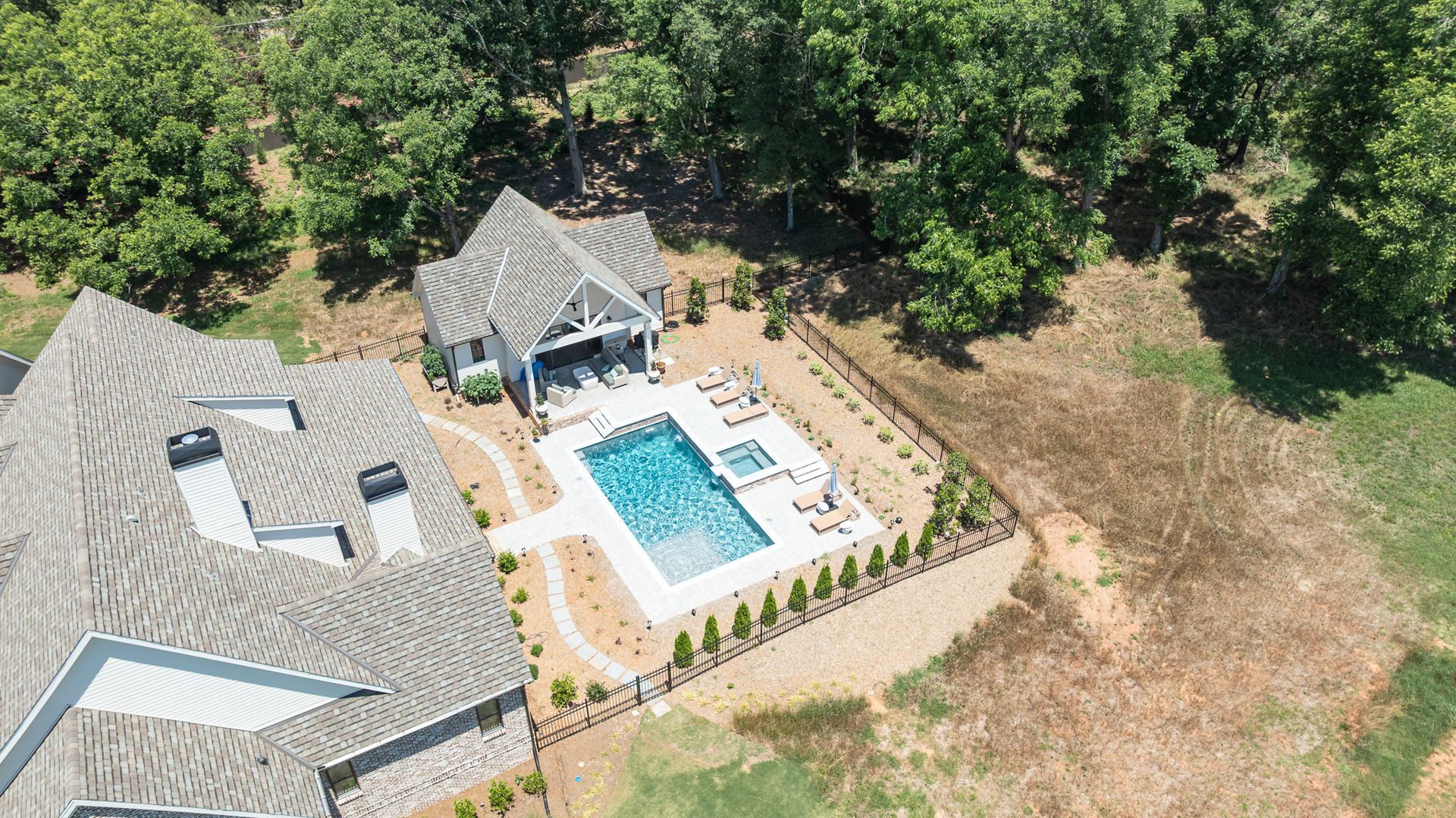 Aerial view of a house with a backyard pool, patio, and surrounding trees