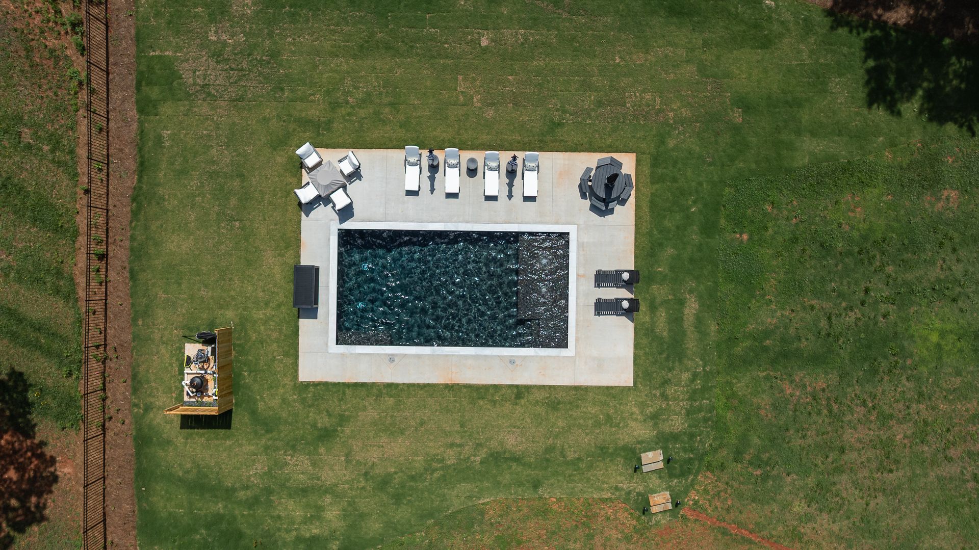 Aerial view of a backyard pool with lounge chairs on a patio and green lawn around it