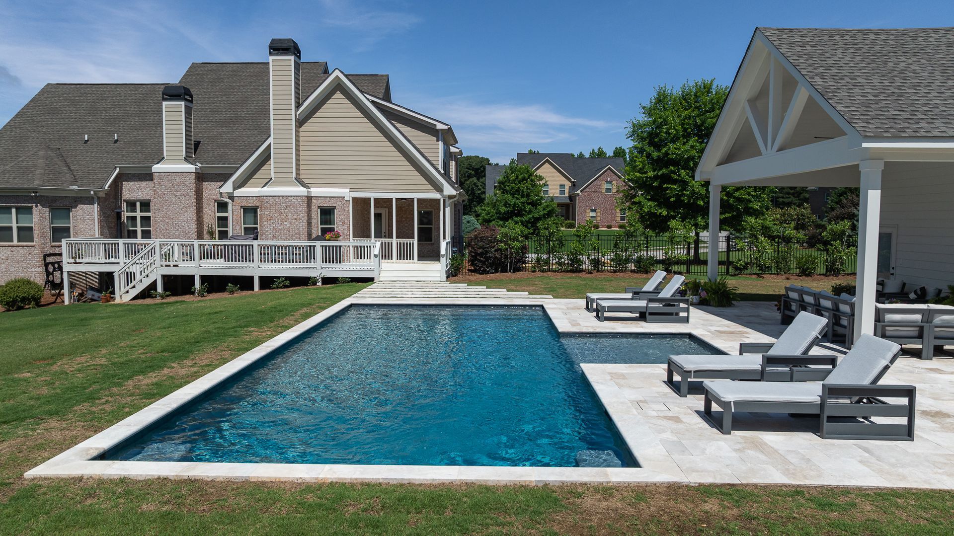 Backyard pool beside a house, with a gazebo and lounge chairs on a sunny day