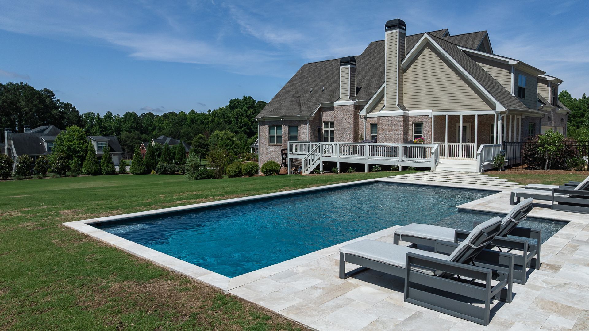 Backyard pool with lounge chairs beside a large house and green lawn
